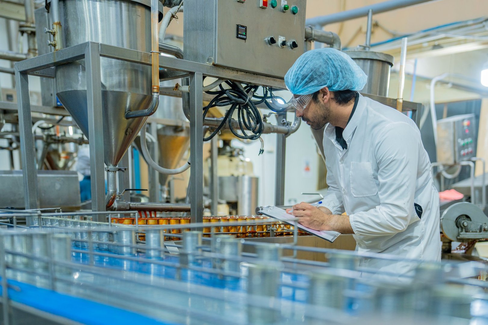 A food quality inspector carefully examines canned goods on a production line, ensuring hygiene and accuracy in an industrial food manufacturing facility.