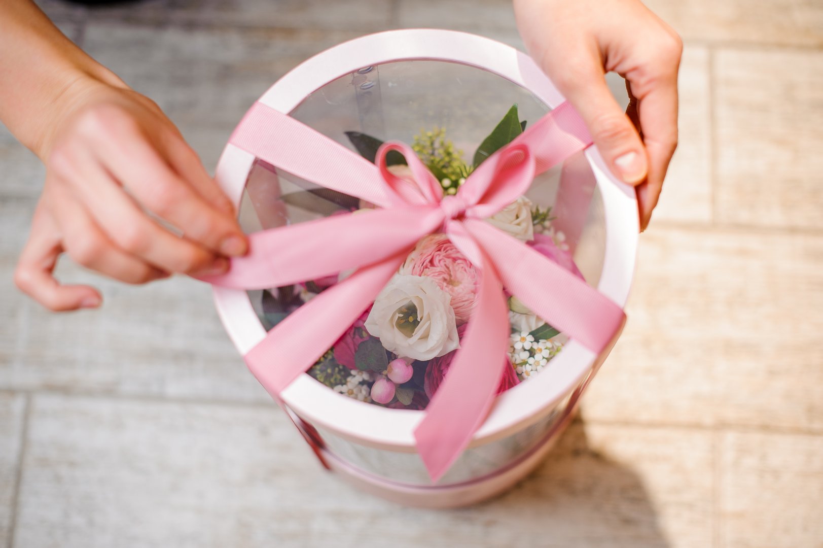 Top view of stylish flower box with cute pink ribbon on the background of wooden floor