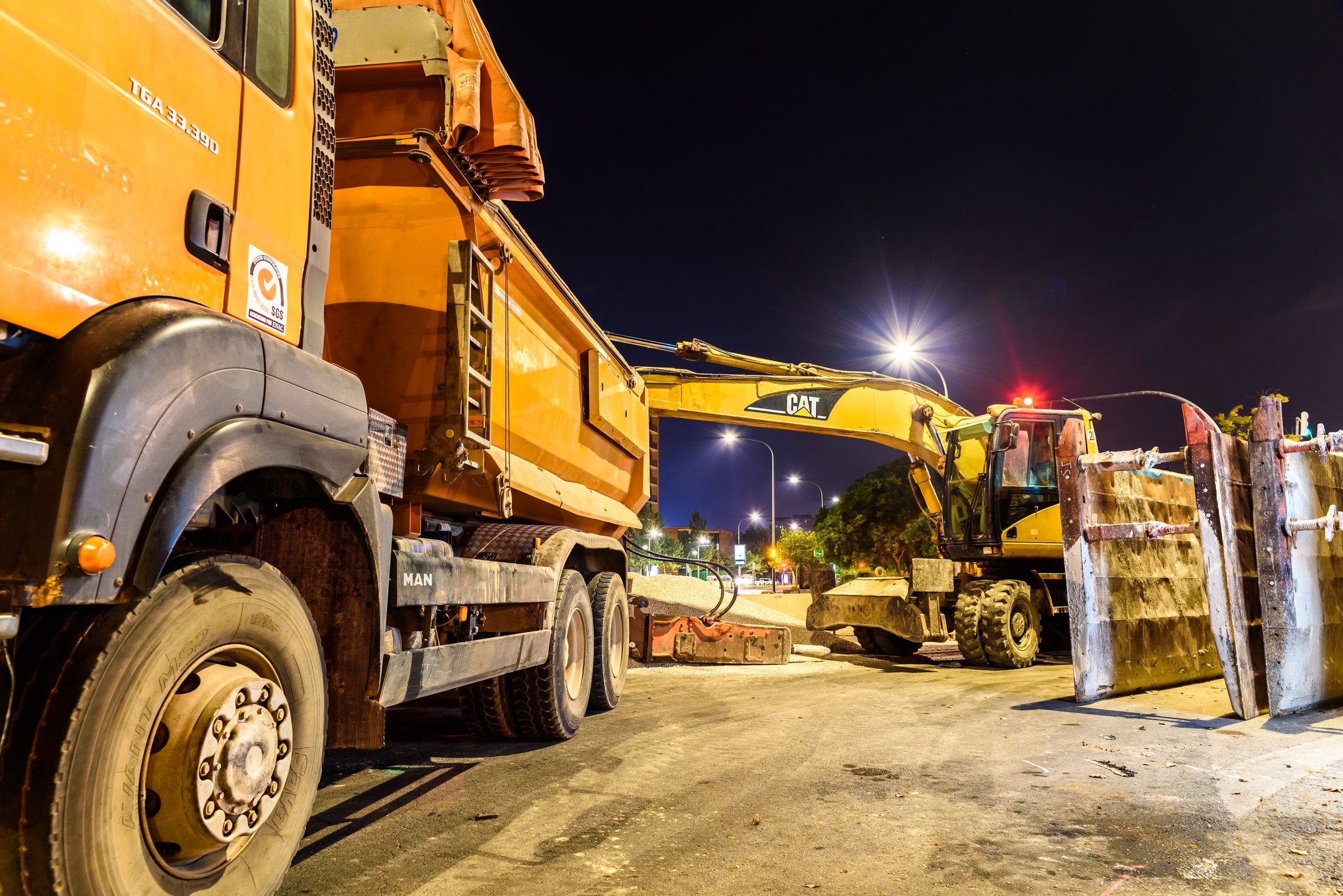 Valencia, Spain - July 4, 2019: A truck next to an excavator parked at night in a sanitation project in a city.