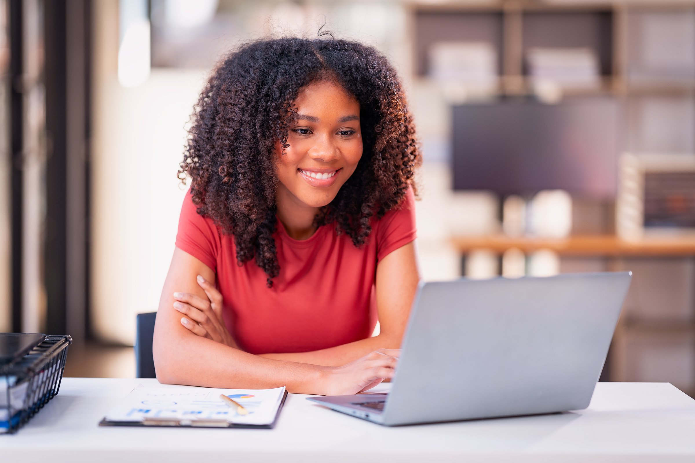 Beautiful professional woman sitting at table smiling while reading important documents with financial graphs and accounting of company.