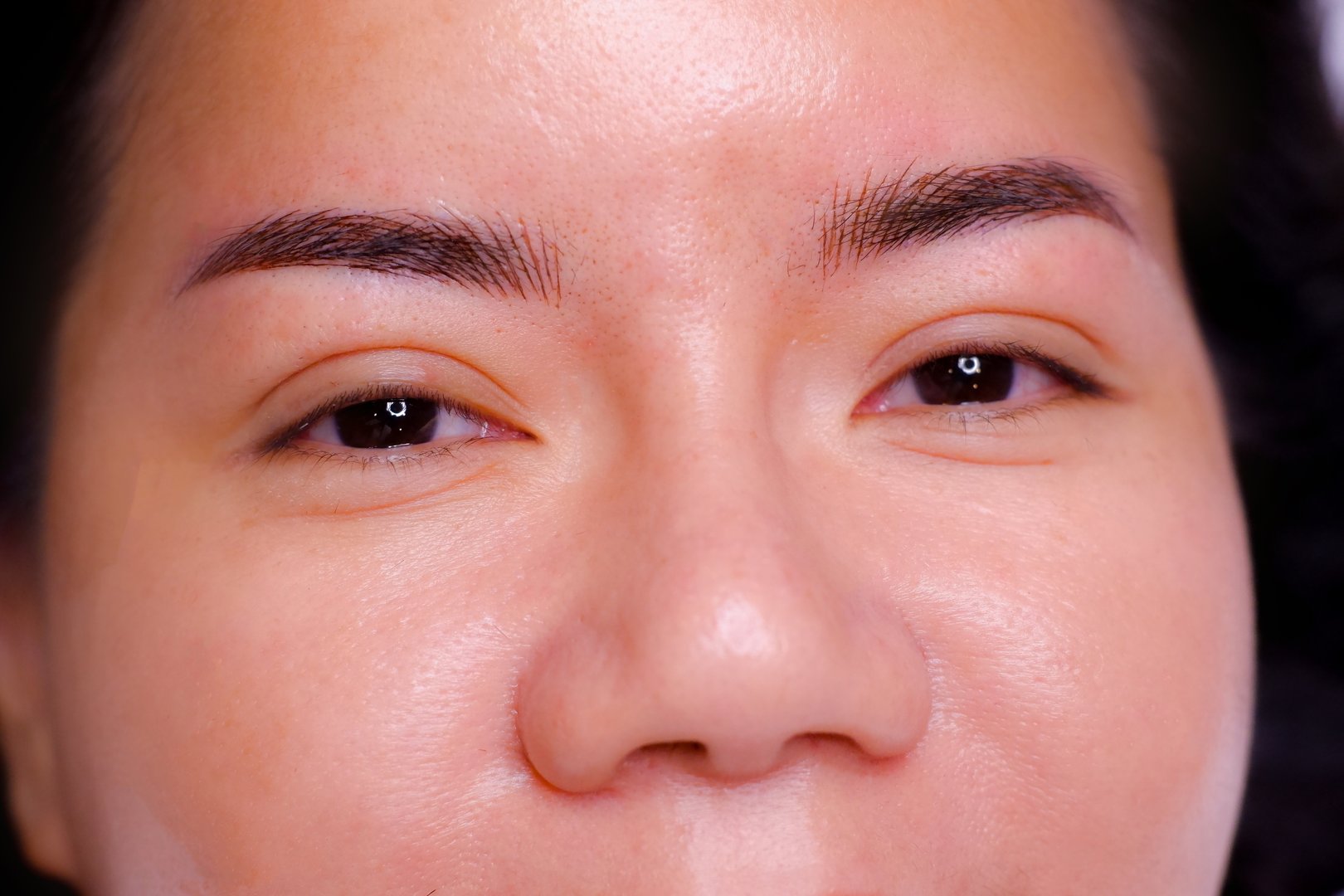 Beautiful female customer after having her eyebrows tattooed by a professional technician. At the eyebrow tattoo shop Beautiful eyebrow lines Asian woman with dark brown hair