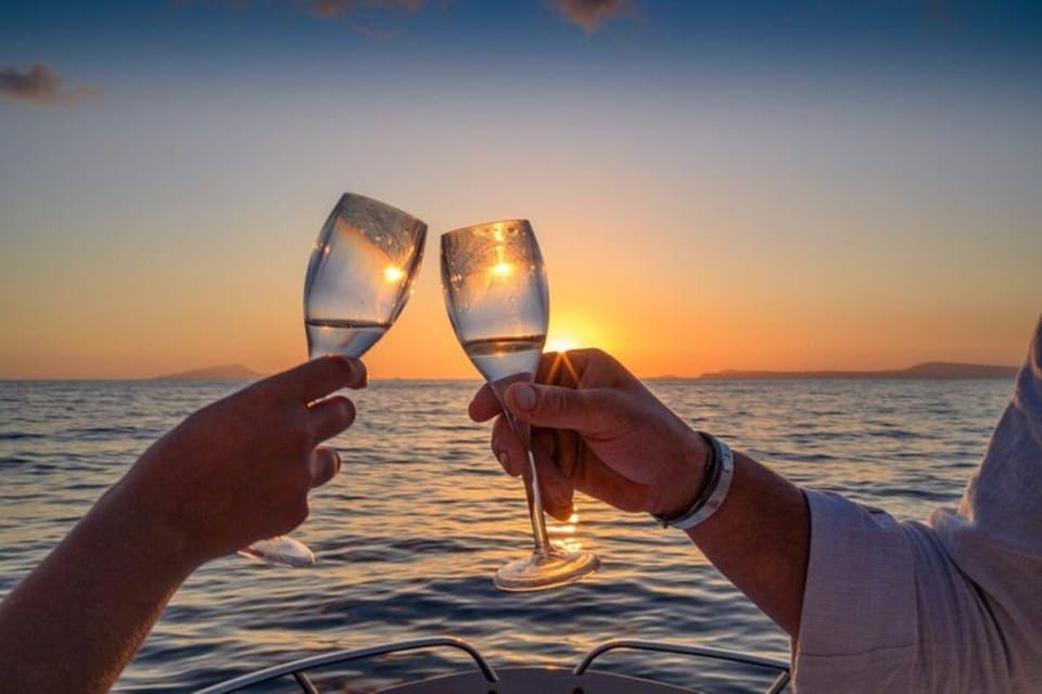 Two people clinking champagne glasses on a boat at sunset, with a golden horizon over calm ocean waters.