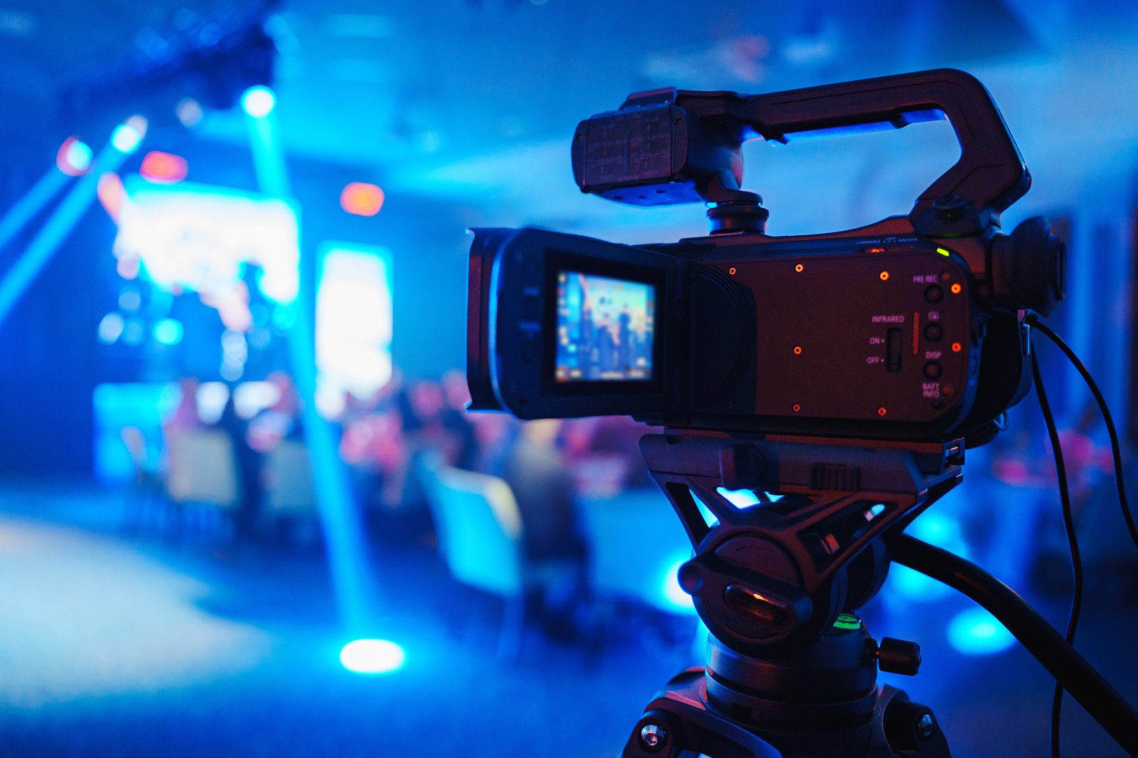 A professional videographer is filming a concert on stage. blurred artists on stage, focus on the camera. unrecognizable people.