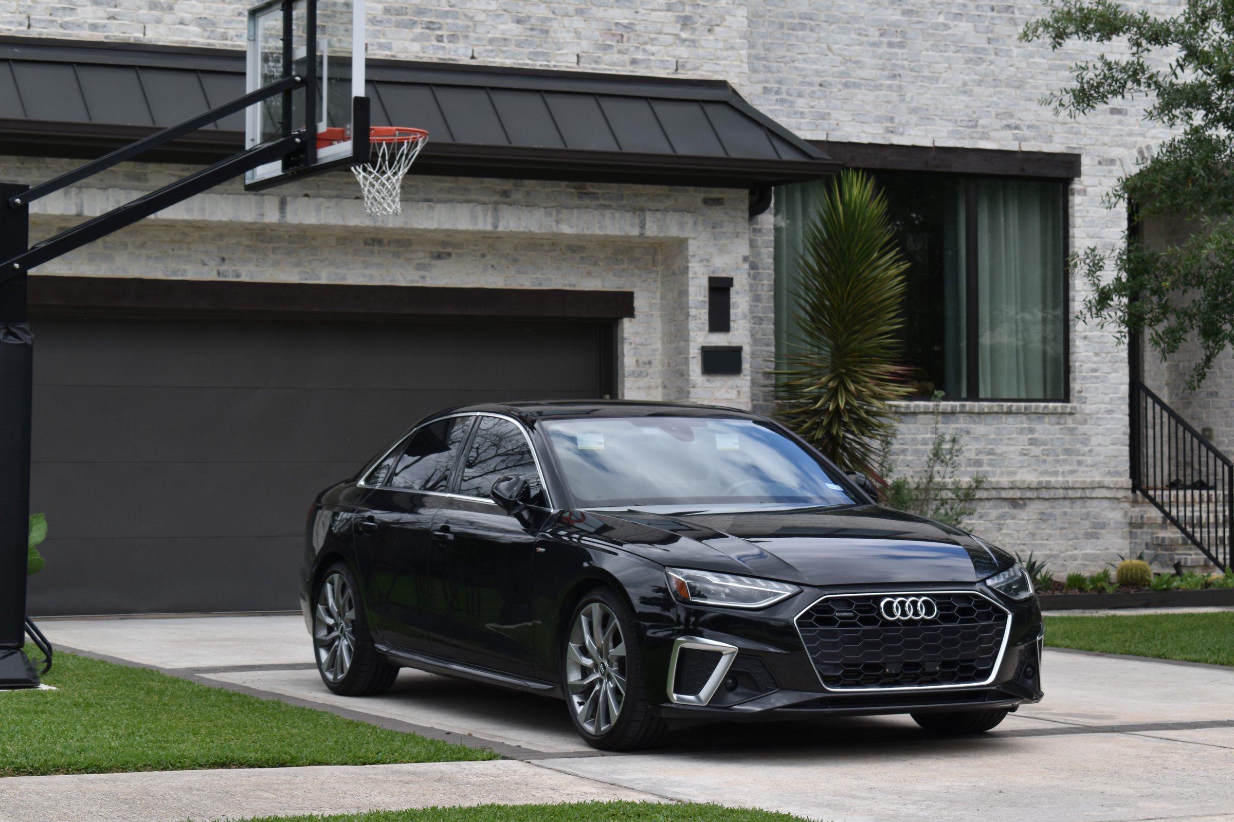Houston, TX USA - 8-11-2023 -A portrait of a luxurious Audi sedan and a splendid home in Houston. In the driveway near the garage is a basketball hoop.
