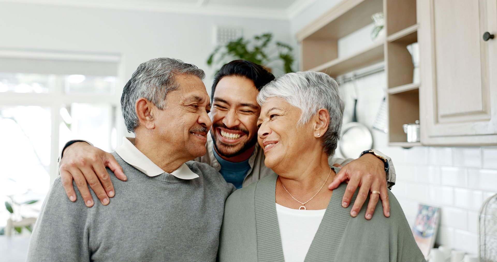 Familia feliz reunida en casa con hijo adulto abrazando a padres en momento de bienvenida