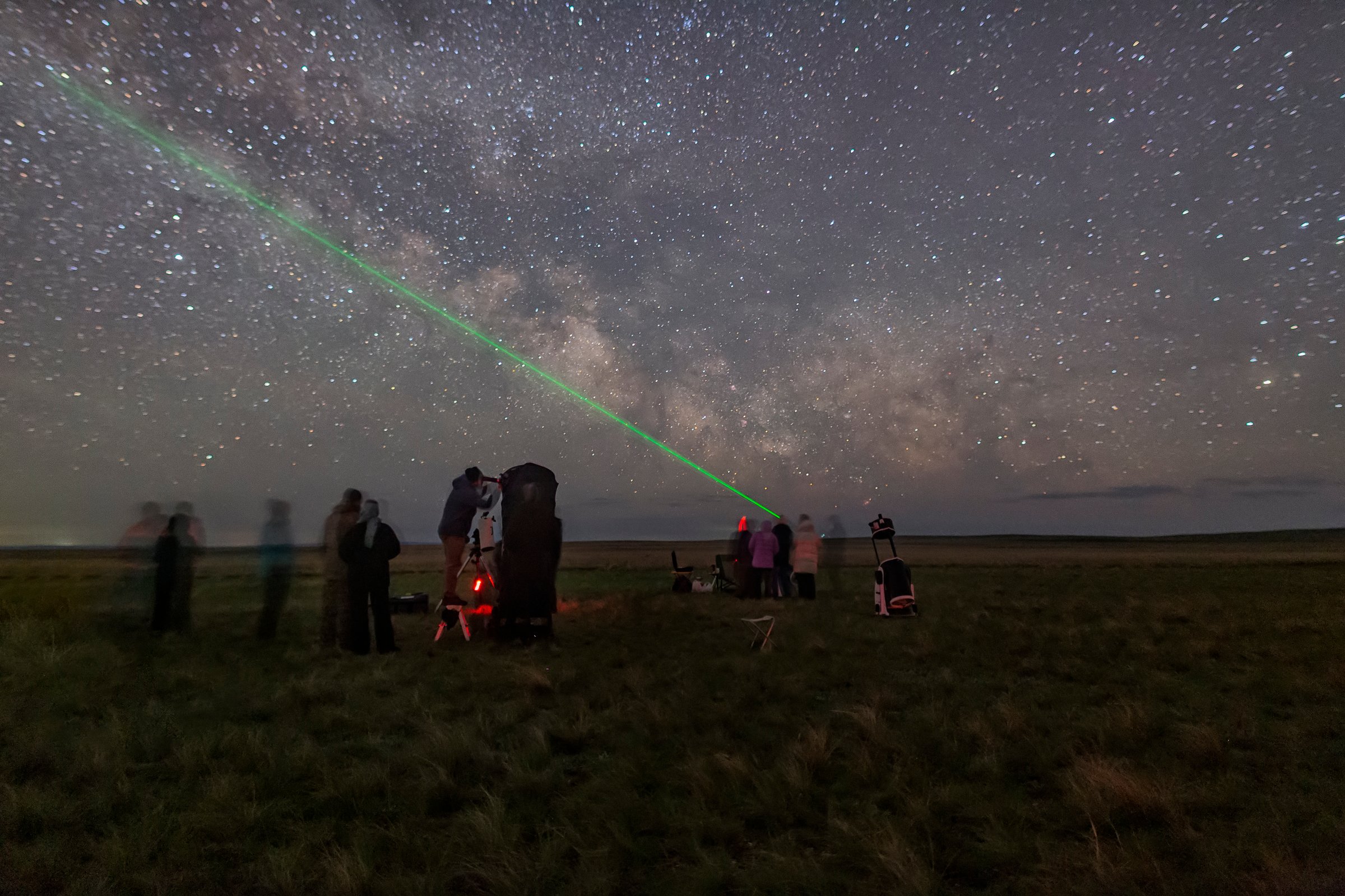 at night there are many telescopes on the astronomical observation site on green grass against the backdrop of the milky way and stars with a green laser pointer. Long exposure astrophotography