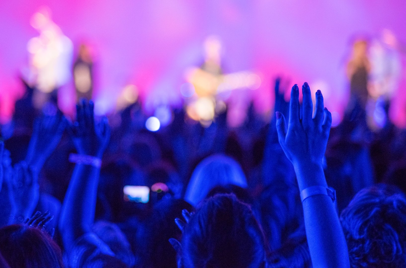 Open hands raised up in foreground with anonymous guitar player on stage in background