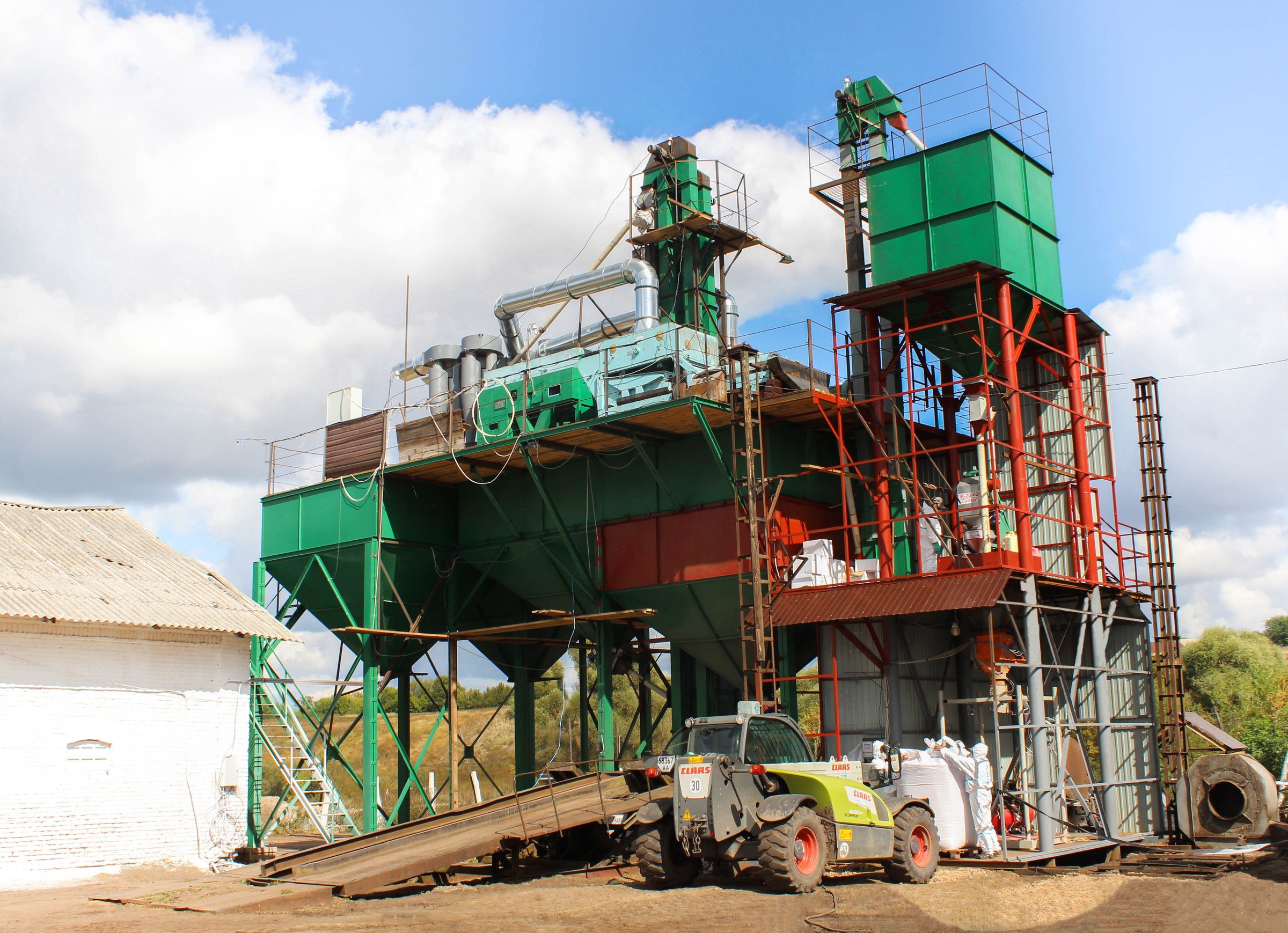 Industrial machinery on a farm, featuring a large green and red grain processing plant with conveyor belts and storage units.