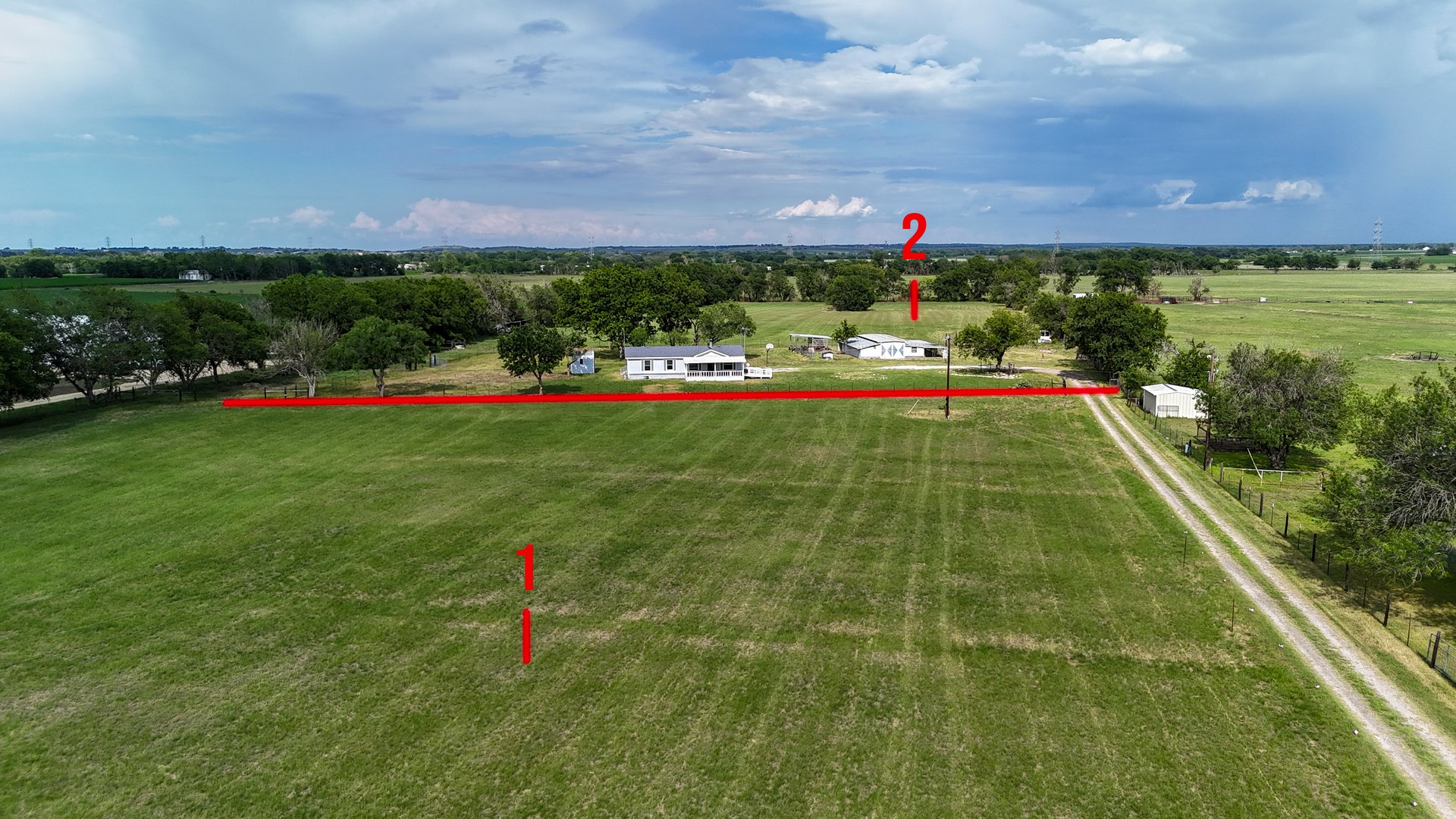 Aerial view of a rural property with a white house, trees, and the landscape marked with numbers 1 and 2 over green fields.
