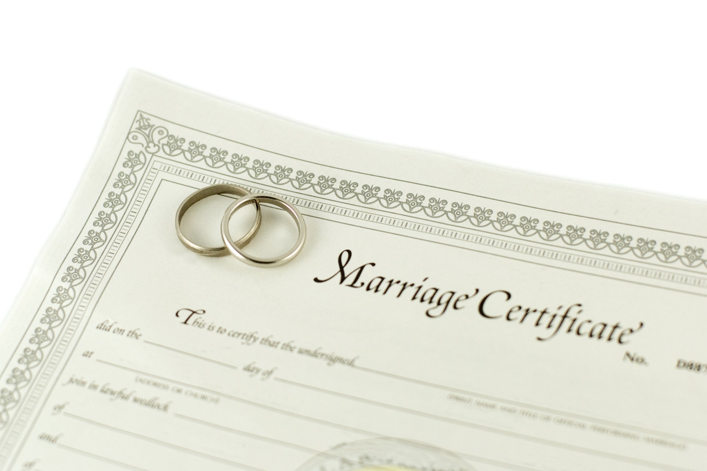 Two wedding rings resting on a marriage certificate with decorative border
