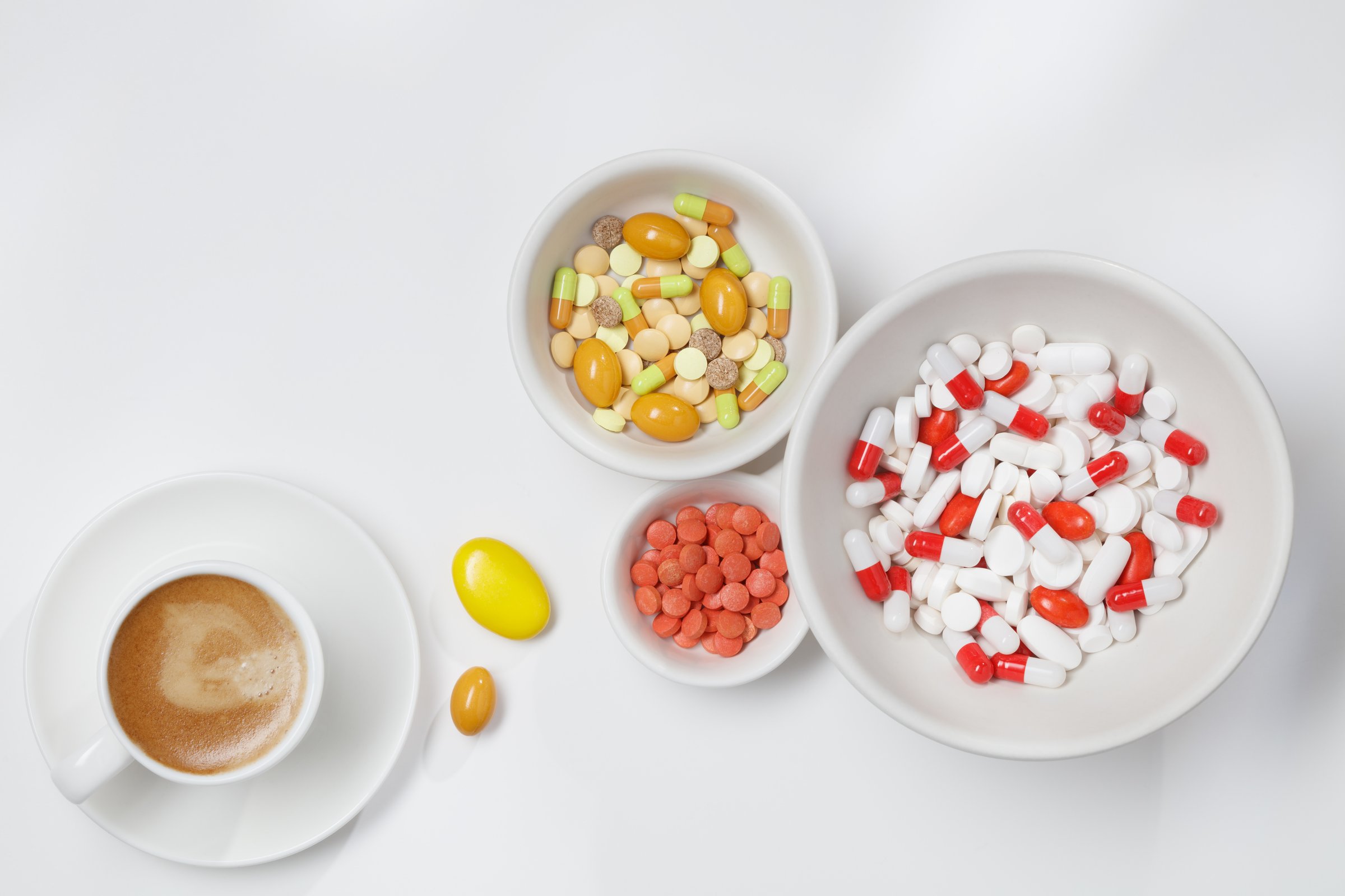 Pills in a bowl and cup of coffee. Multi-colored tablets in bowls on white background. Flat lay. Bowl of medicine caplets.
