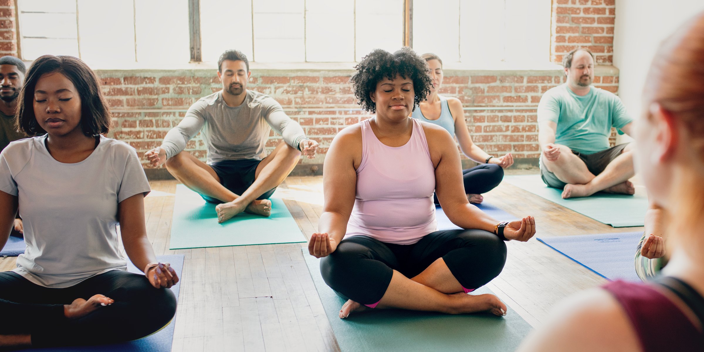 Diverse group of men and women practicing yoga. The yoga class includes various ethnicities, with participants sitting on yoga mats. Yoga for relaxation and fitness. Exercise and yoga for well being.