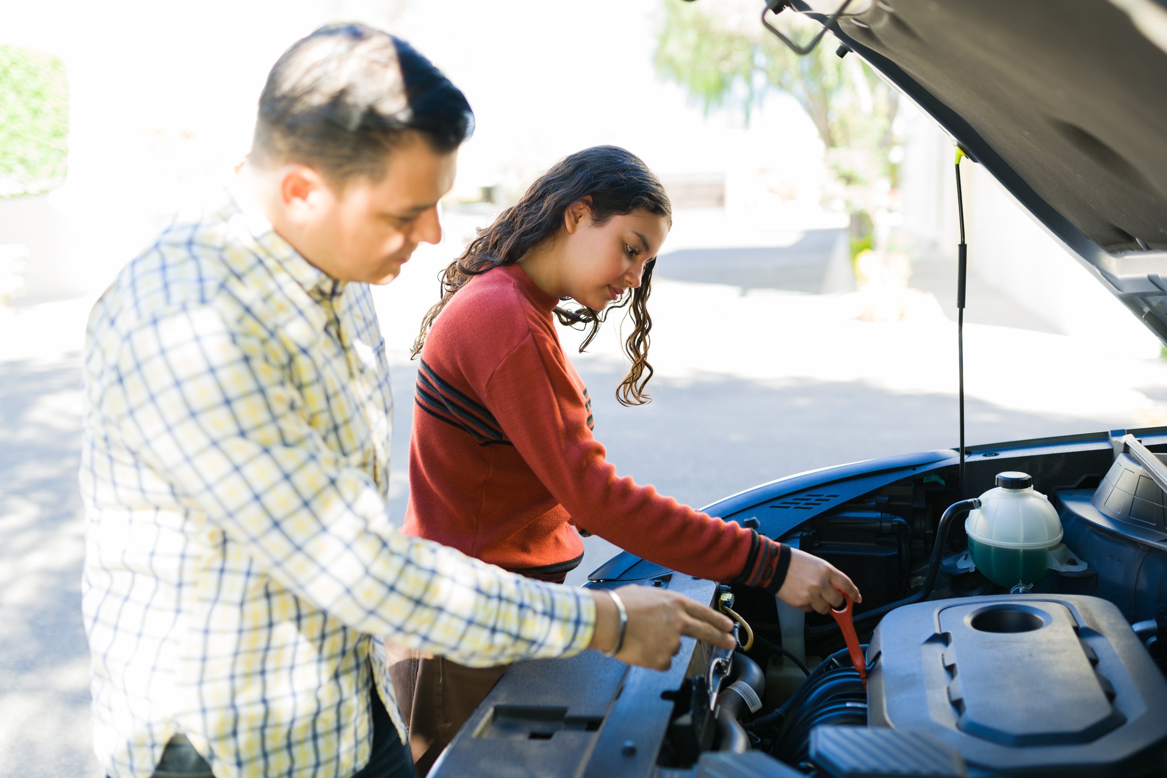 Father teaching his teenage daughter how to check the oil level in a car engine - hispanic family bonding over car maintenance