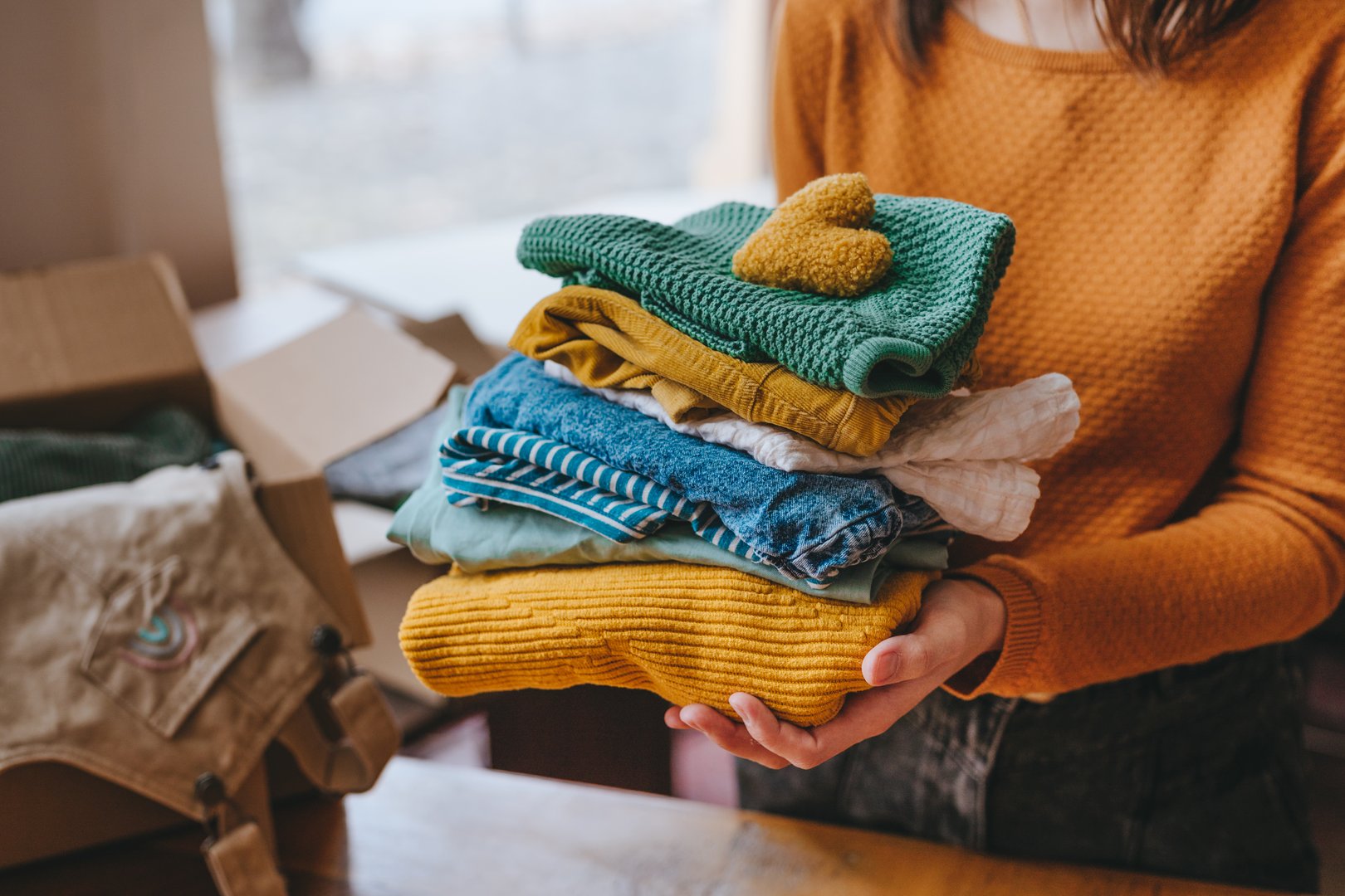 Close-up of female hands holding a fabric heart and clothes for charity. Upcycling concept.