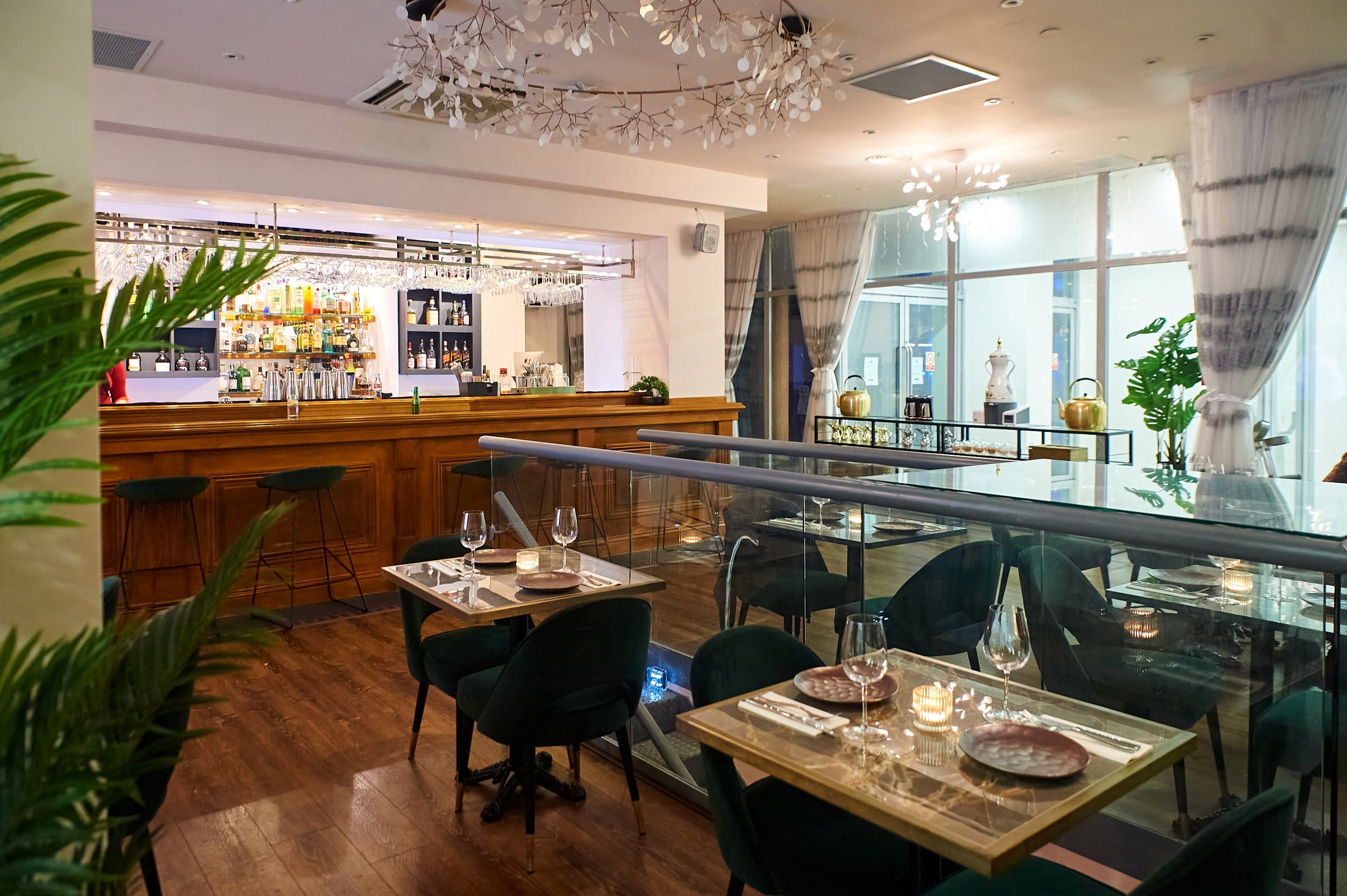 Elegant restaurant interior with wooden bar, tables set for dining, and stylish lighting accents.