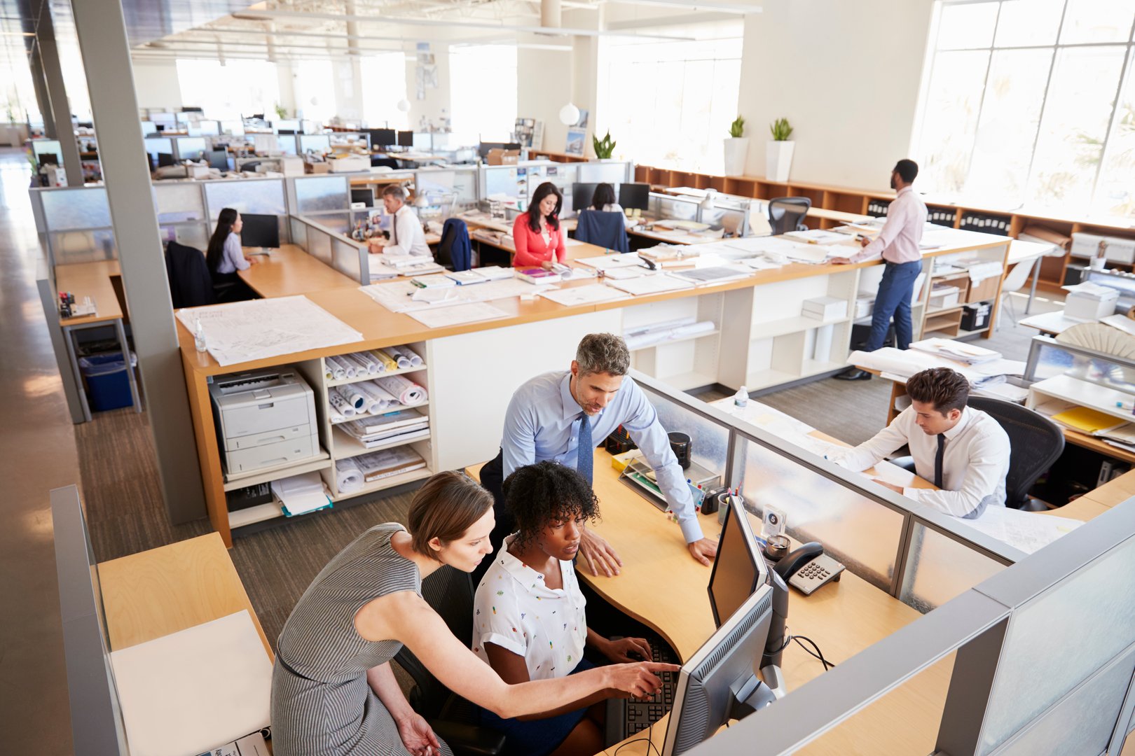 Colleagues working at a woman's workstation in a busy office