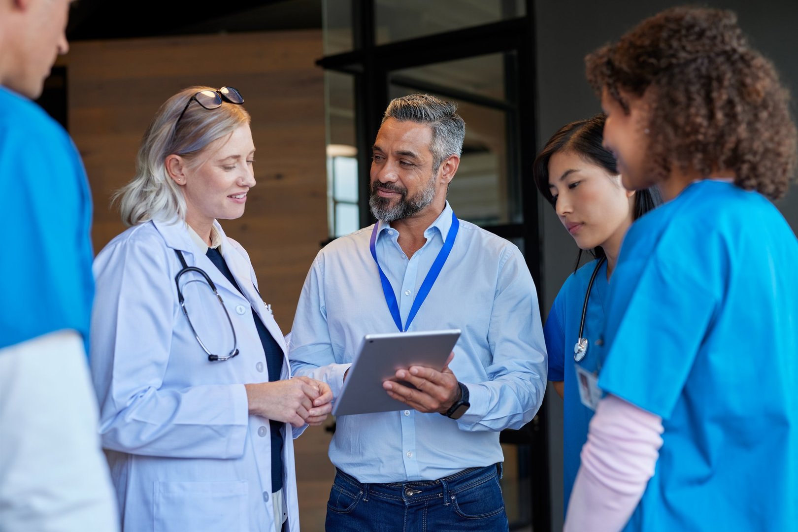 Medical mixed race team consulting with pharmaceutical representative at hospital hall. Healthcare hospital staff reviewing new pharmaceutical information. Doctors and nurses discussing healthcare advancements with businessman.