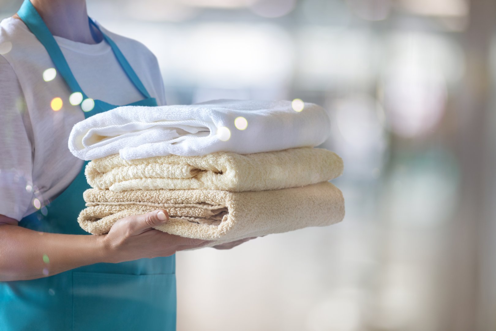 A cleaning lady holds a stack of clean towels on a blurred background.
