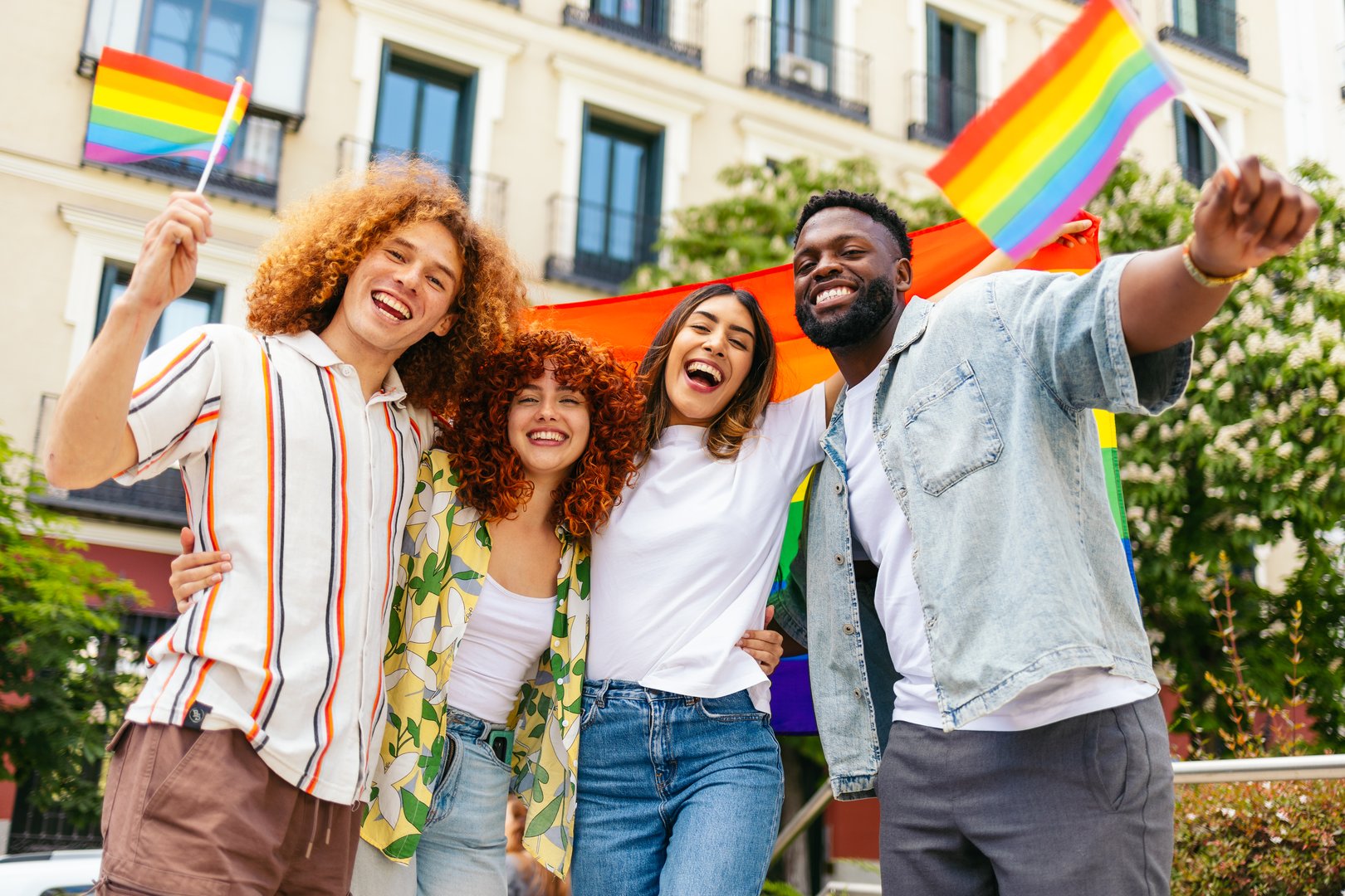 Multiracial friends hugging and waving rainbow flags while celebrating lgbt pride month