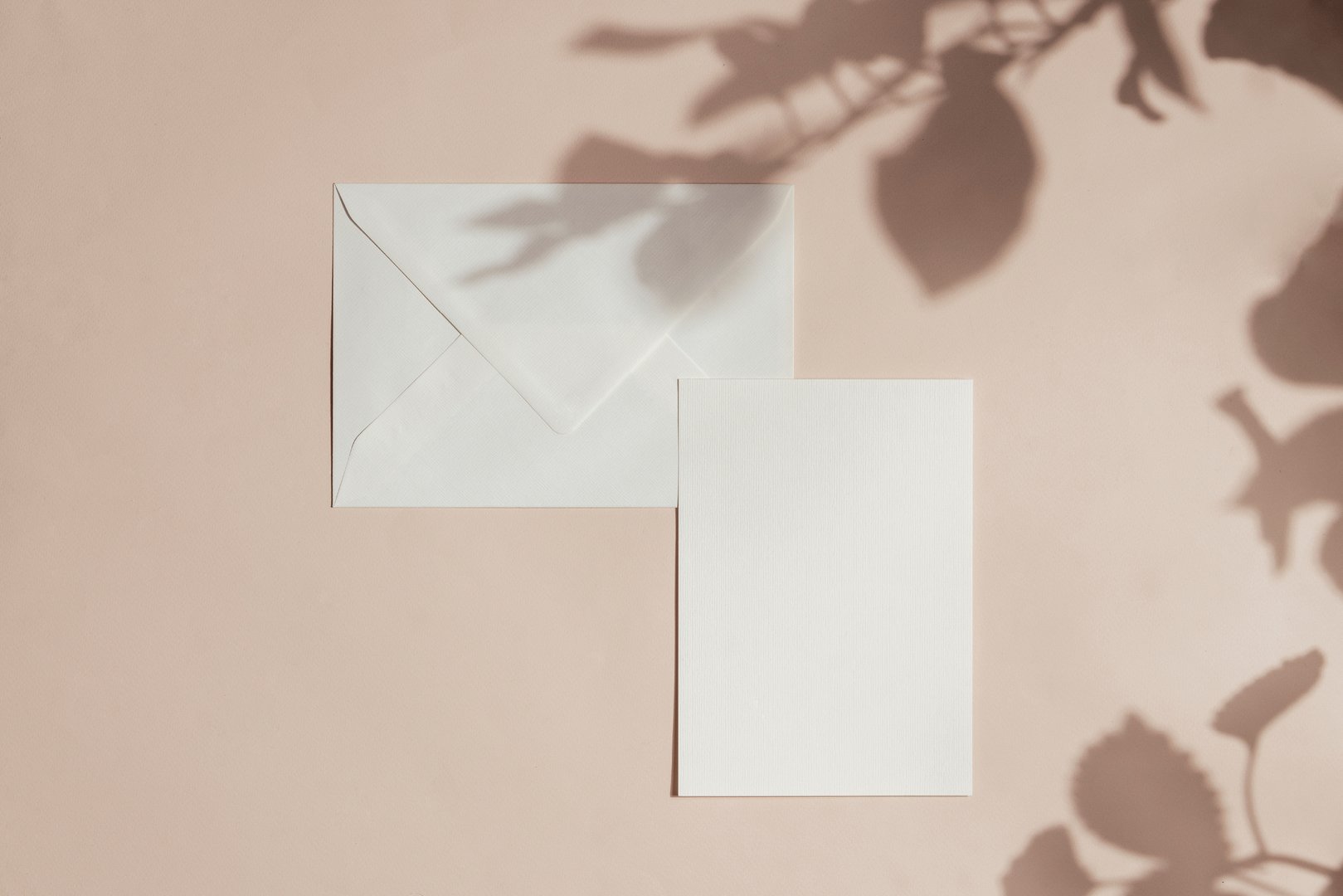 Feminine  wedding, birthday stationery card, envelope mockup . Blank greeting card, envelope. Pink pastel beige background, flat lay, top view, flower shadow, natural light.