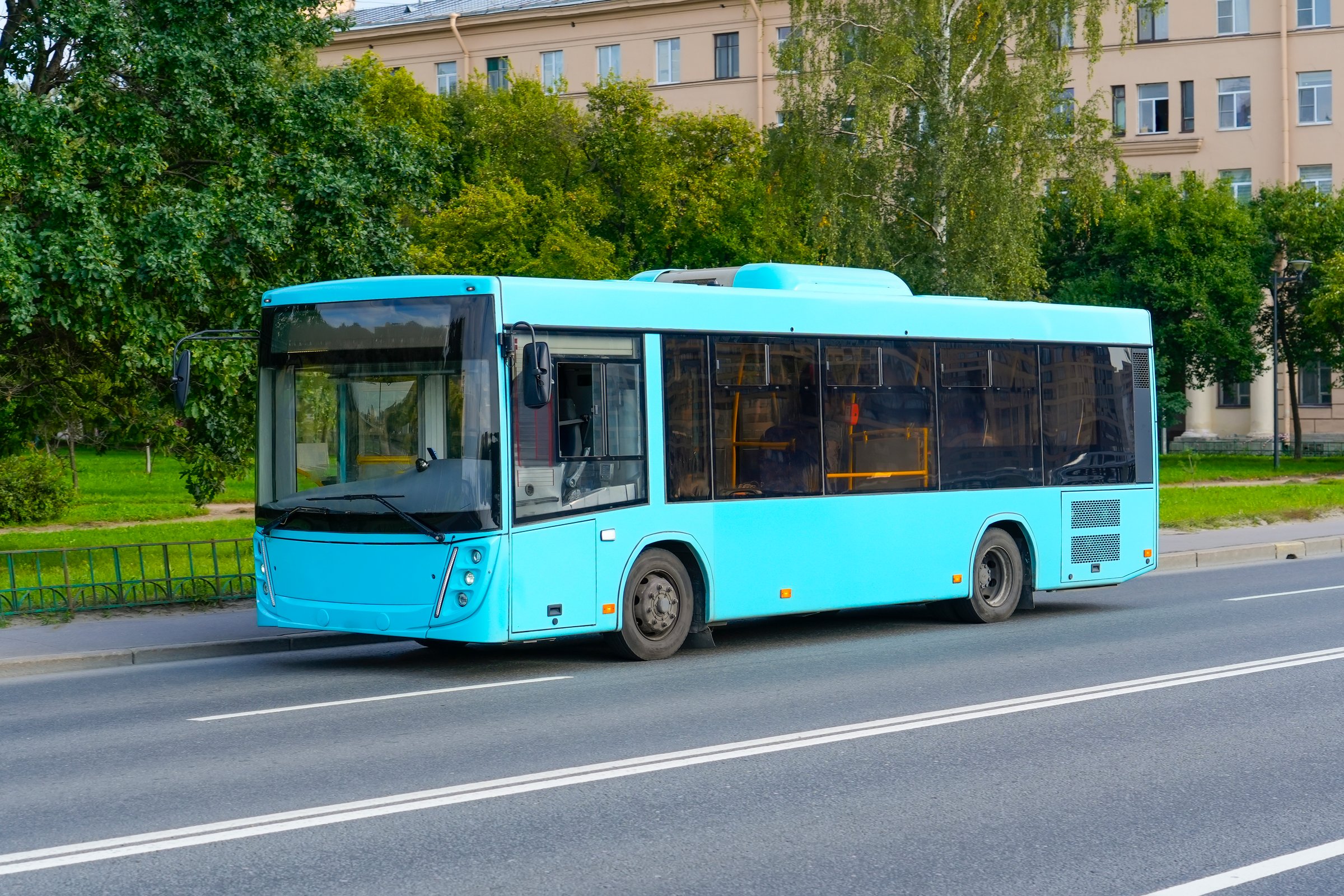 Blue azure bus riding on the road in city green trees street