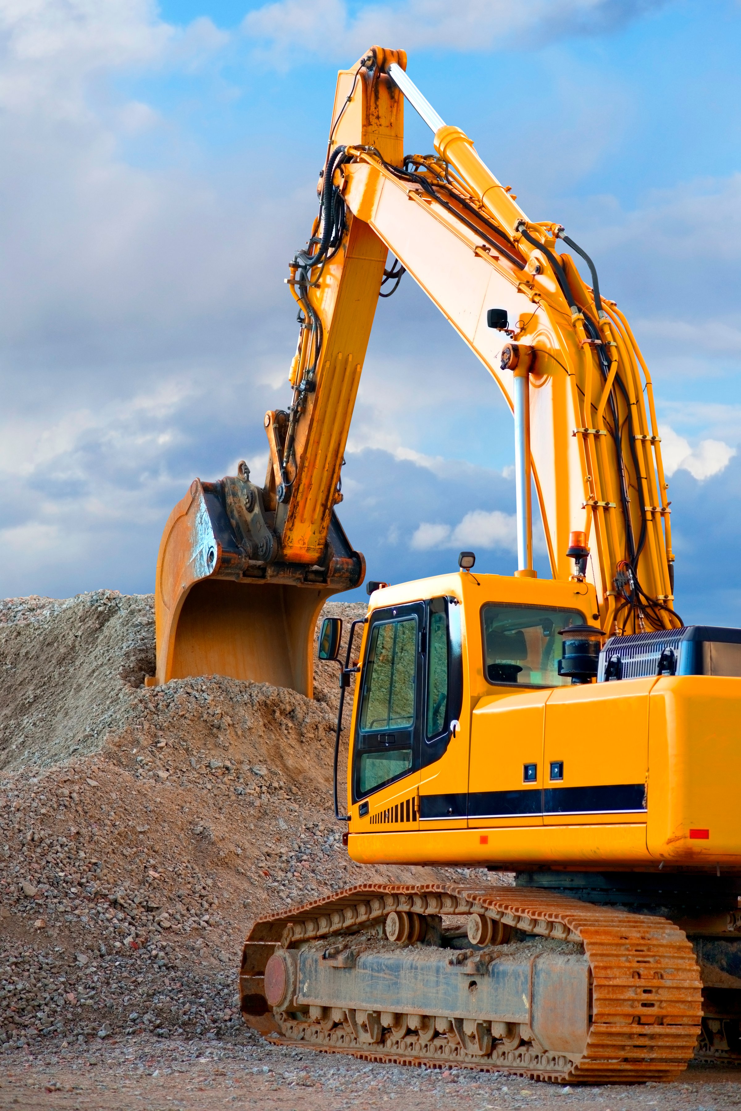 Yellow digger with big heap of gravel on blue sky