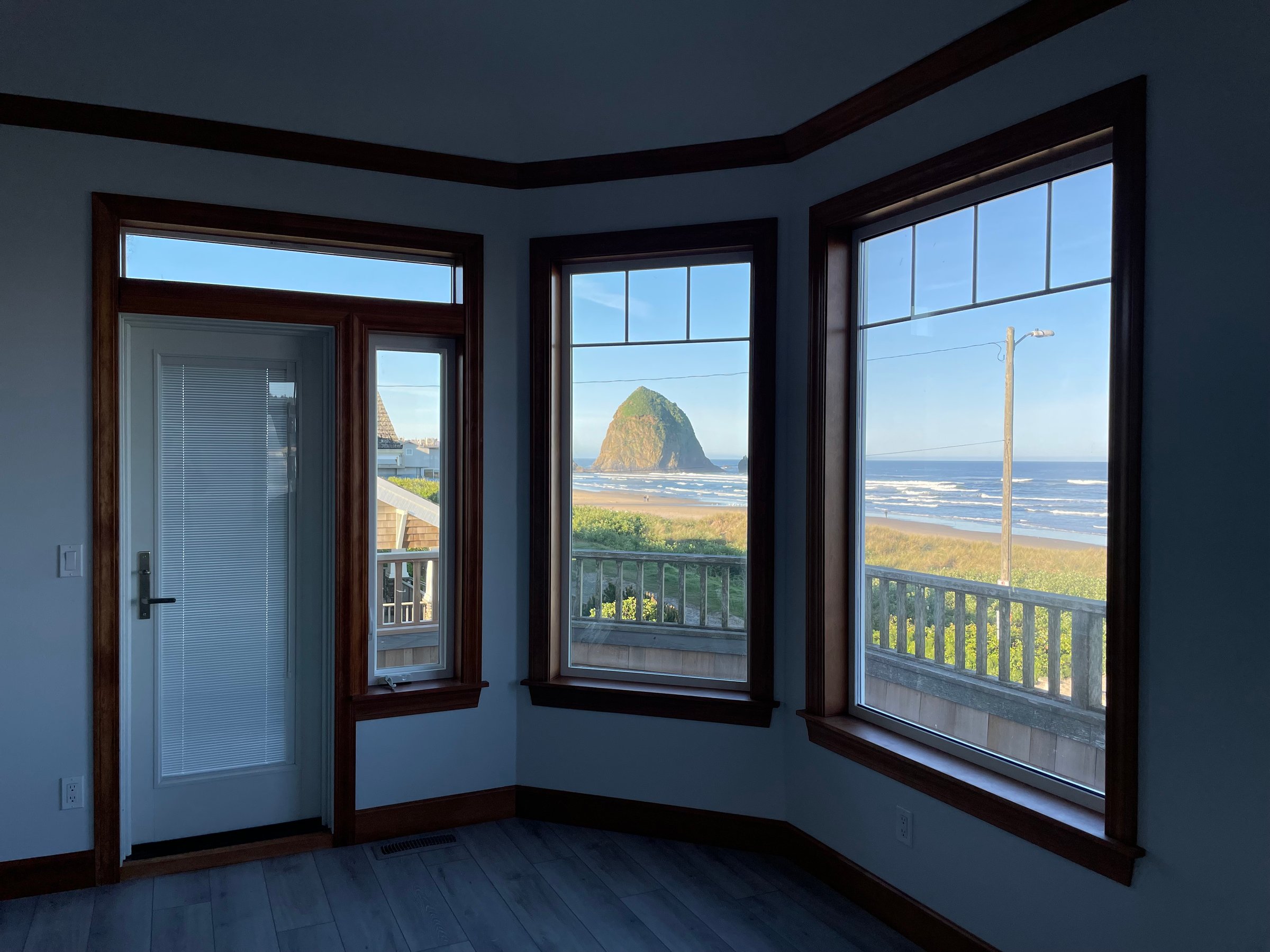 Room with large windows and a glass door overlooking a beach with a distinctive rock formation in the distance.