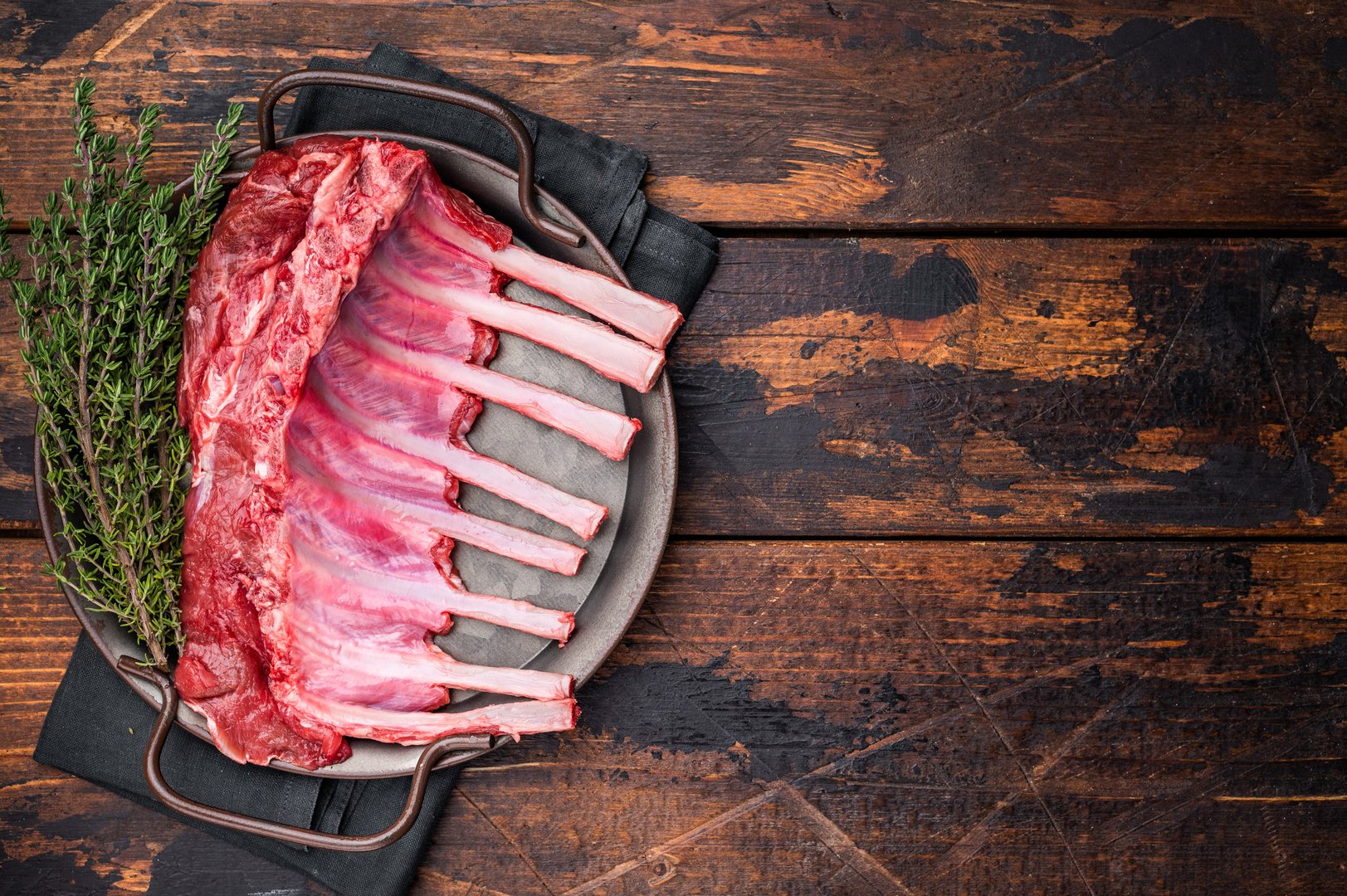 Fresh rack of lamb, raw mutton meat for chops steaks on steel tray. wooden background. top view.