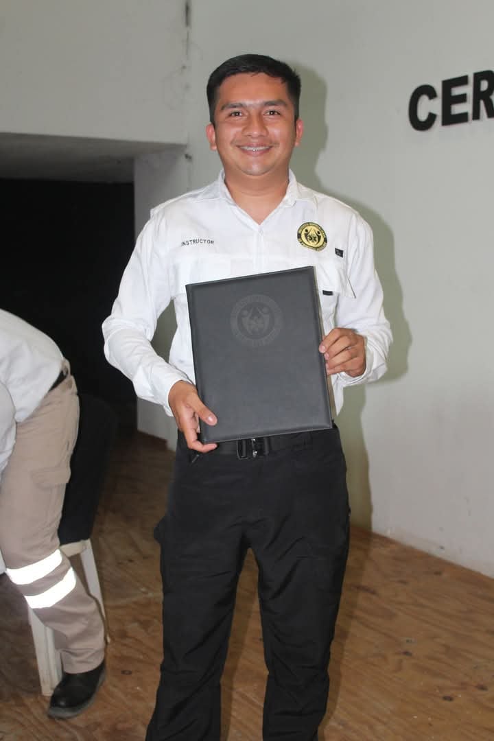 Smiling man in uniform holds a black diploma folder during a ceremony.
