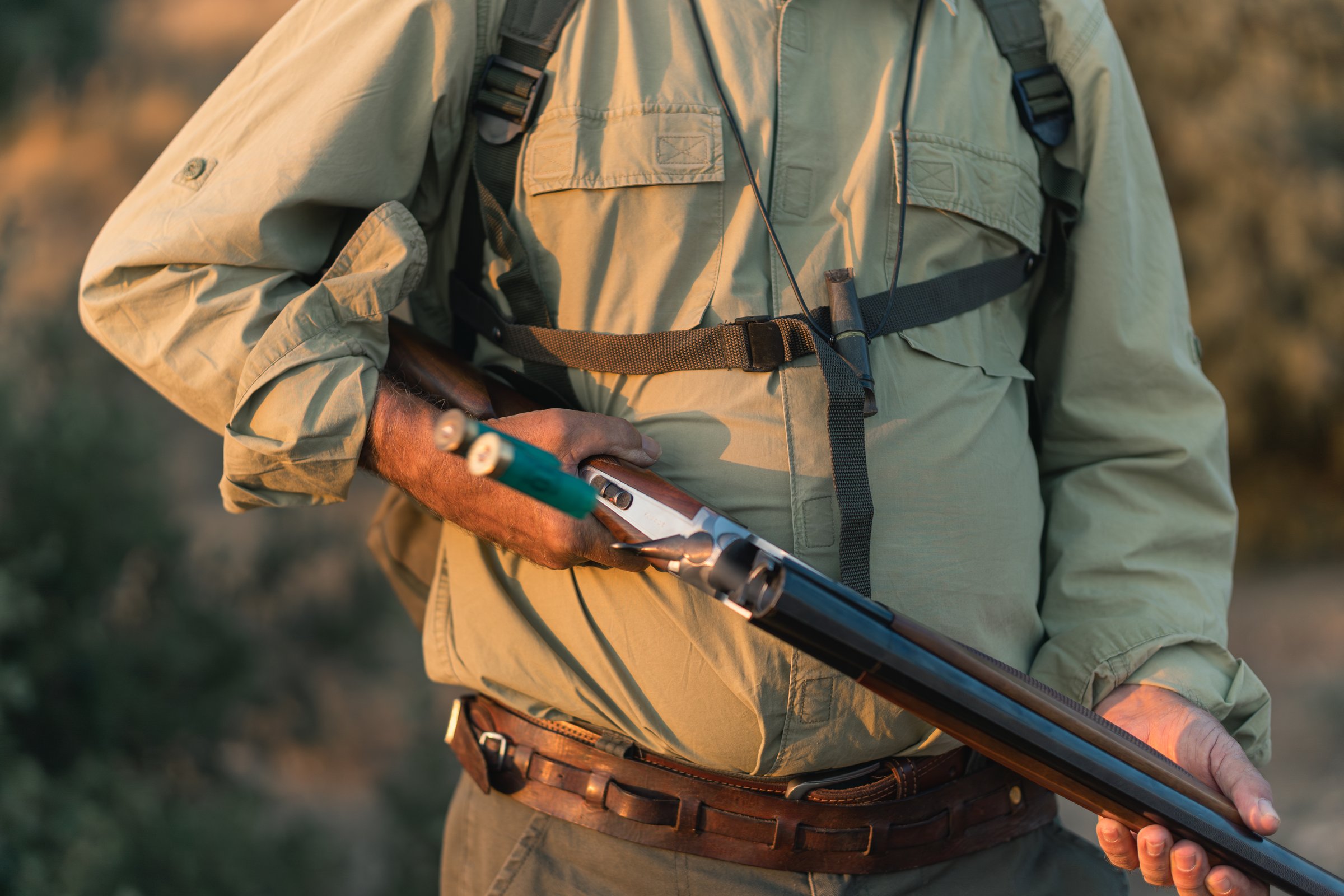 Senior hunter holding a shotgun outdoors during golden hour