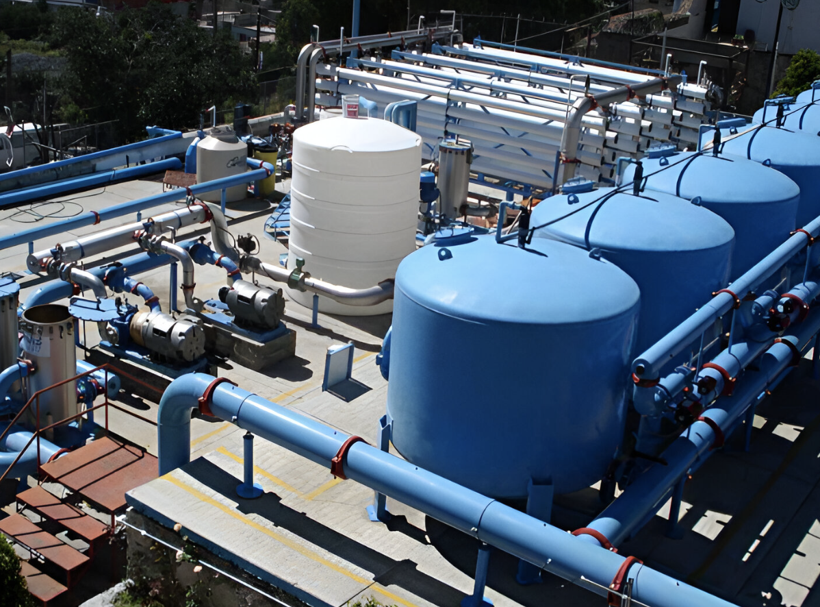 Industrial water treatment facility with large blue tanks, pipes, and filtration equipment outdoors.