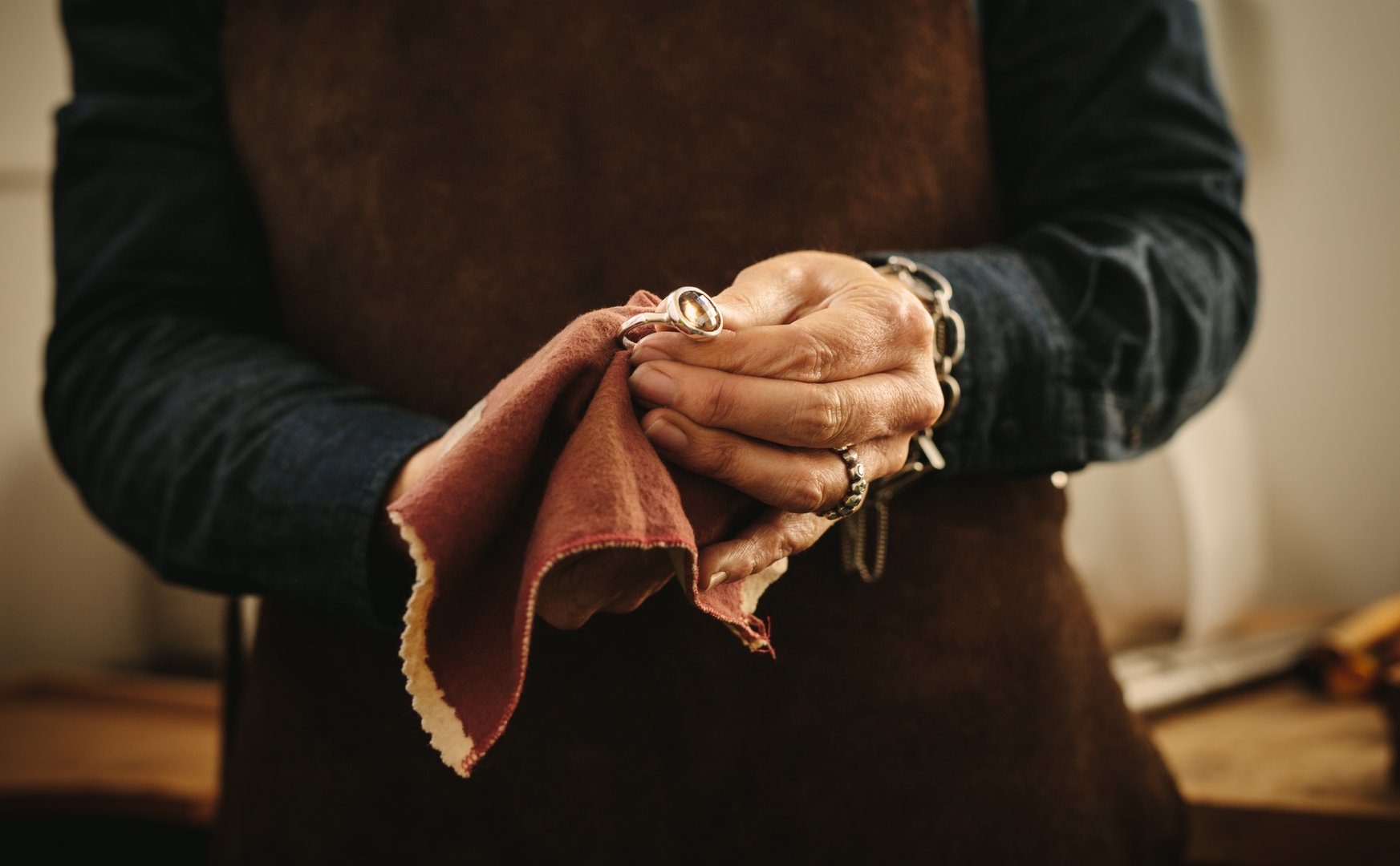 Hands of female jeweler polishing silver old-fashioned jewelry with a cloth. Jewelry maker wiping a ring with cloth at her workshop.