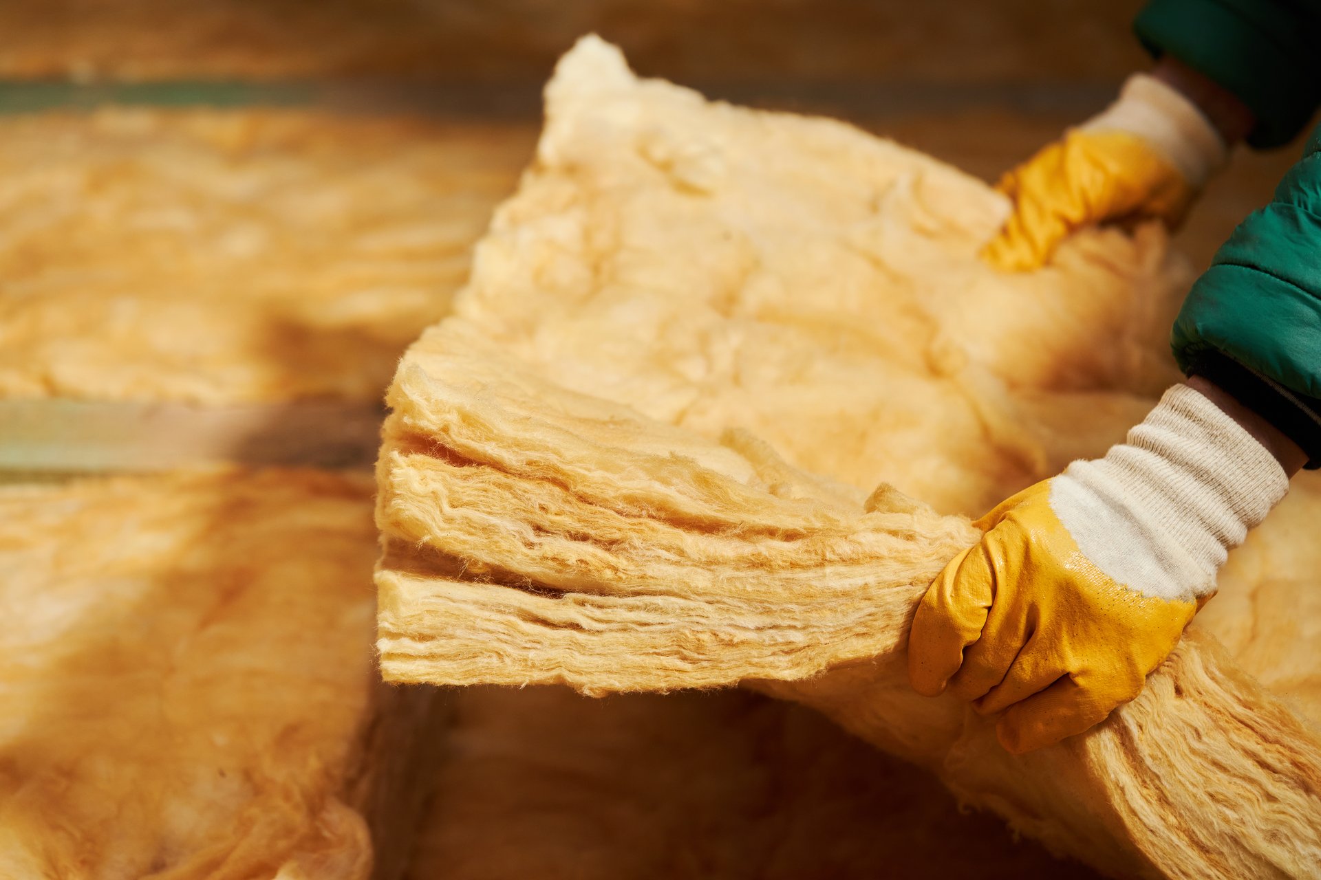Construction worker thermally insulating house attic with glass wool.  Attic renovation and insulation concept