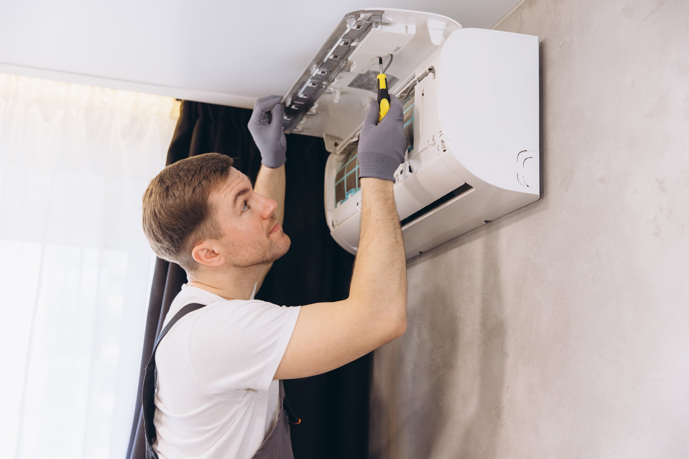 Plumber using screwdriver and wearing gloves repairing an air conditioning unit in a modern home