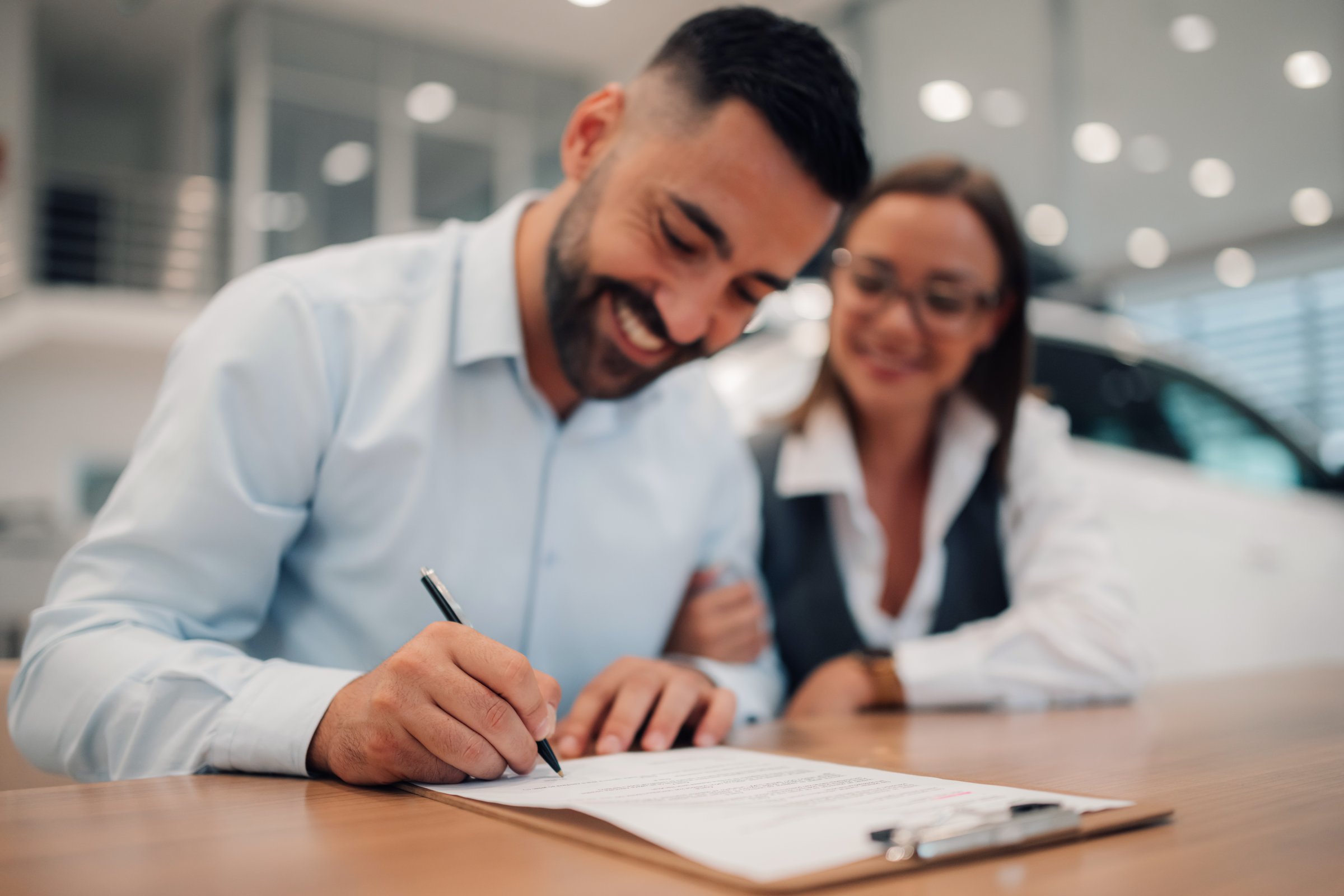 Happy couple smiling and signing a contract for their new car in a dealership, finalizing the purchase and excited to drive it home
