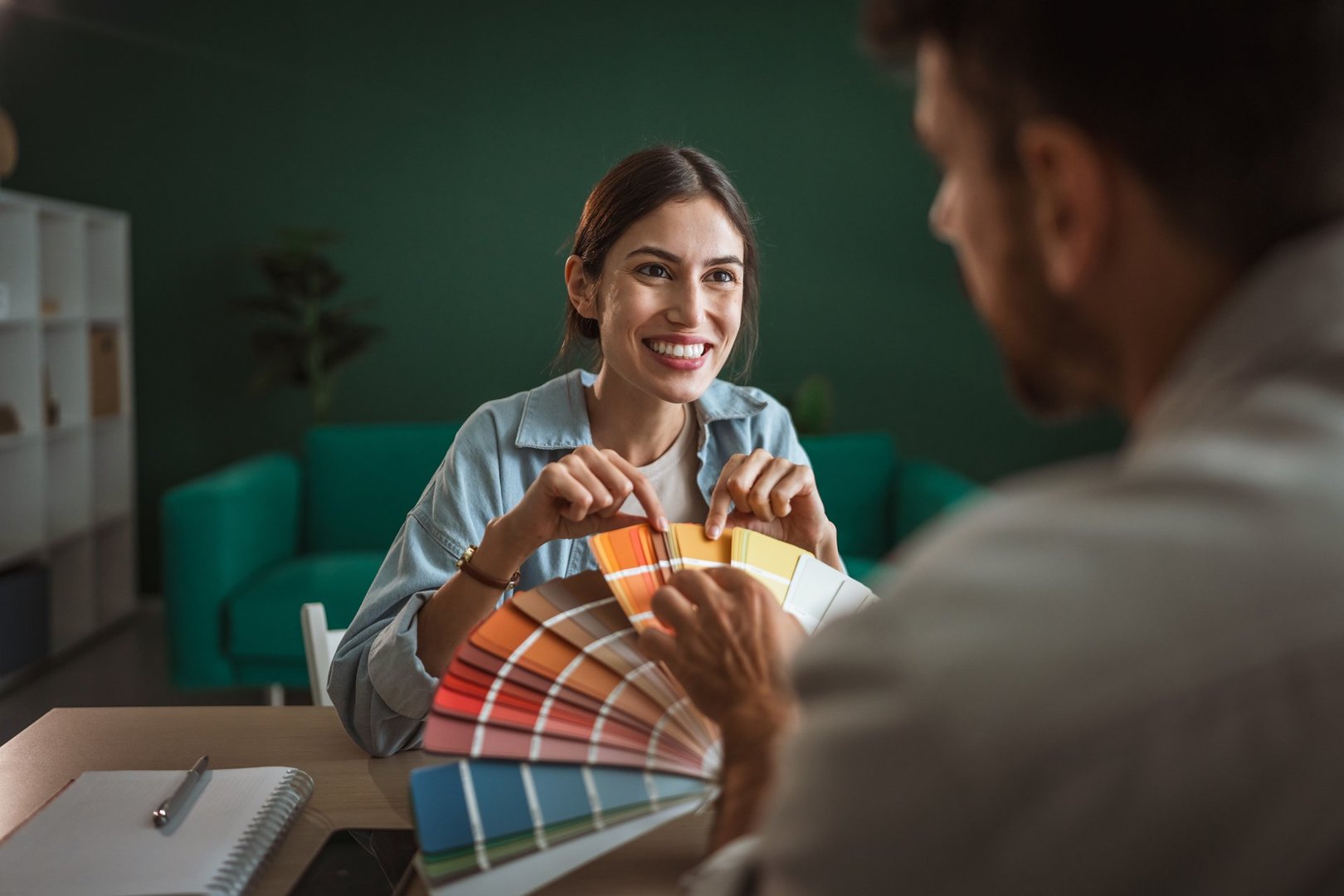 Young woman smiling while pointing at color swatches on a fan deck, discussing paint choices for an interior design project or home decorating with a man