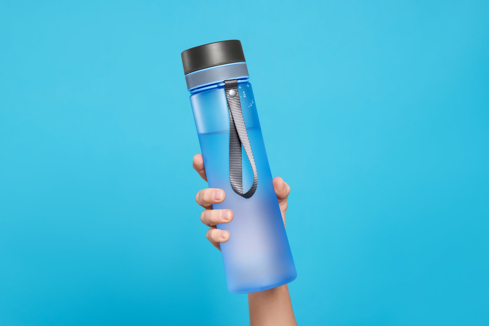 Woman holding bottle of drink on light blue background, closeup