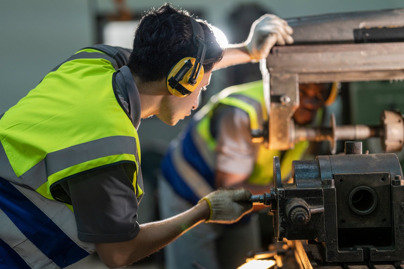 A skilled technician works attentively on a heavy duty machine in an industrial workshop. Dressed in safety gear, he demonstrates focus, precision, and craftsmanship in a professional environment.