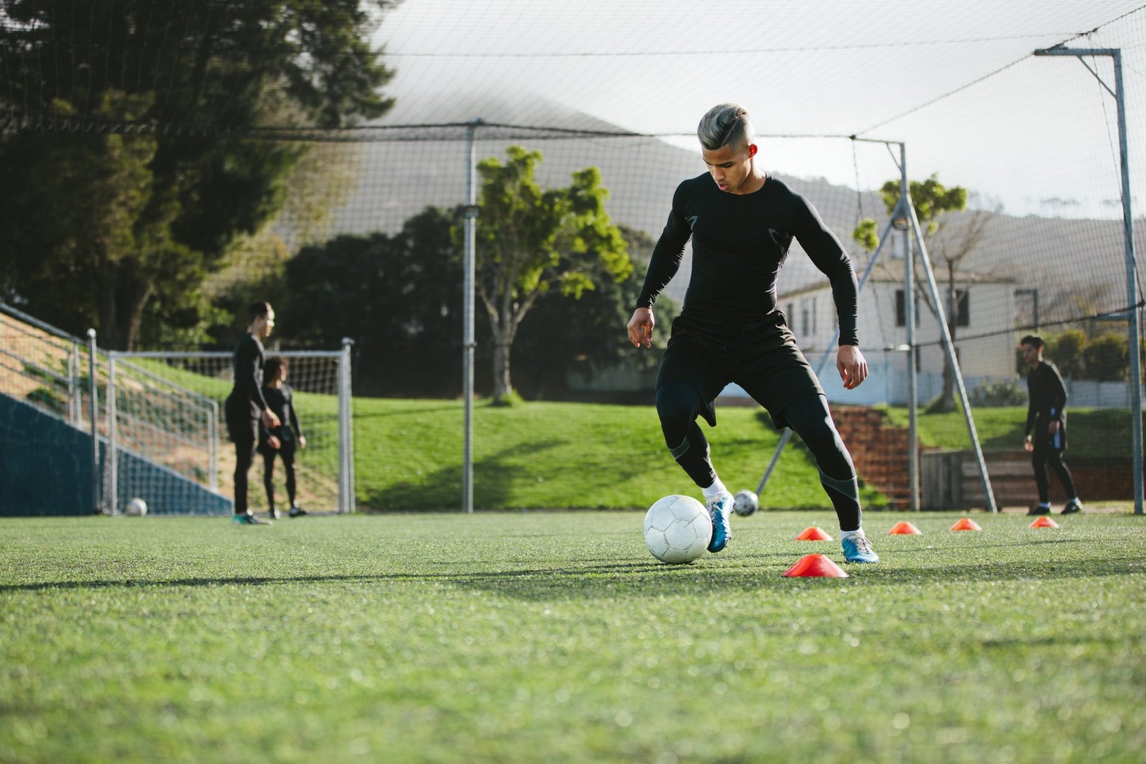 Young soccer player training in football field with team in background. Five a side football team practicing on field outdoors.
