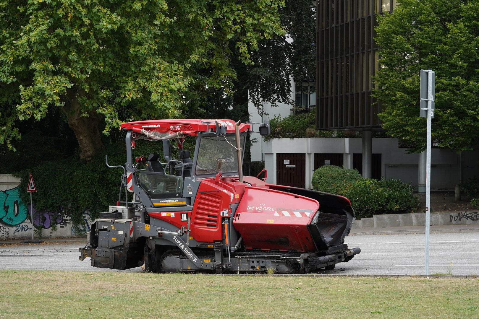 Hamburg, Germany 08 27 2022: Red tracked paver without driver is parked on the street ready for overlay work with road asphalt on an existing surface. Behind are some administrative buildings.