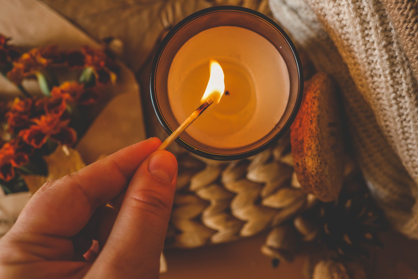 Close-up of a hand lighting a red candle with a match.