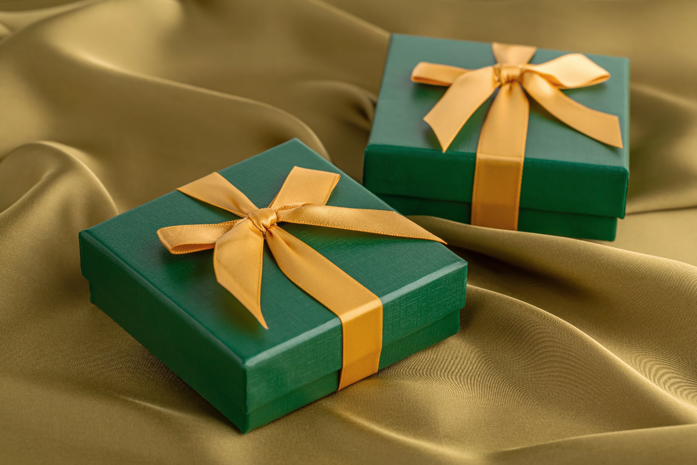 The green and yellow gift boxes with ribbon on the yellow silk background.