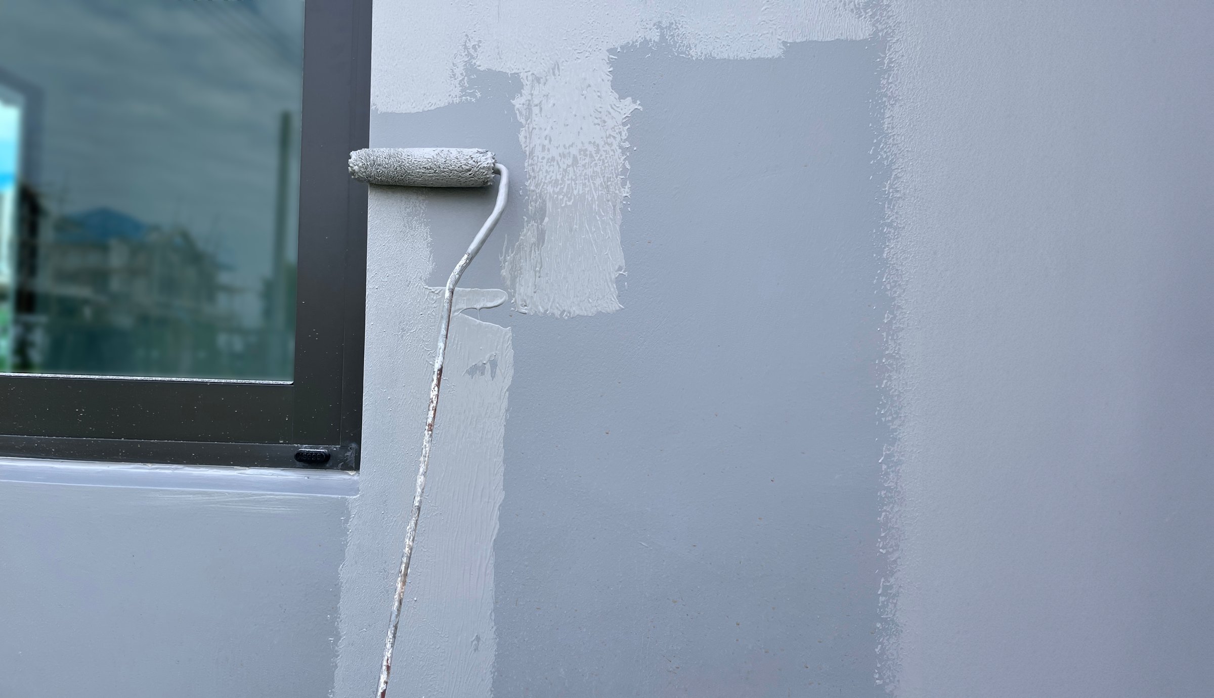 A worker is painting the walls of the house with a primer using a paint roller.