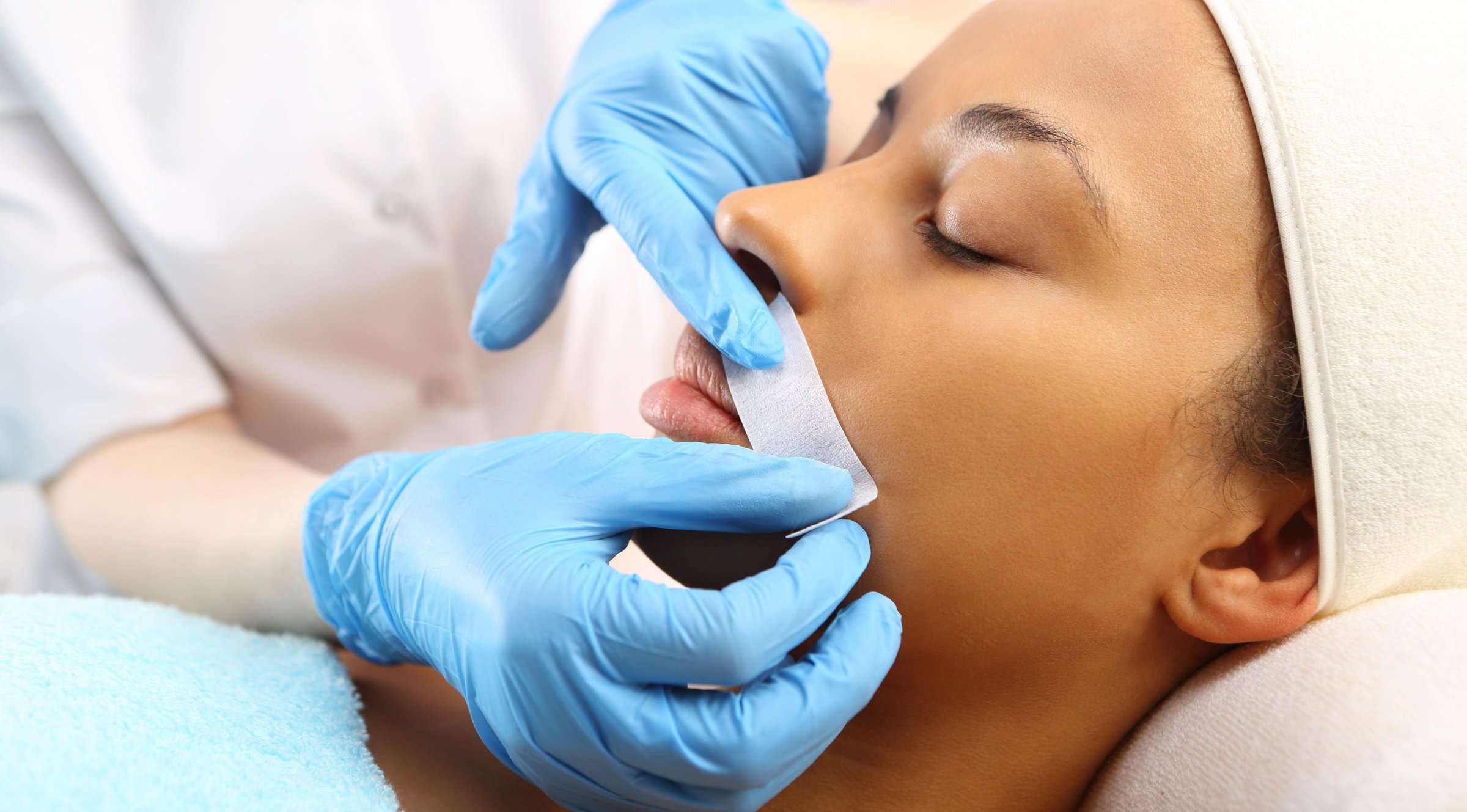 Close-up of a person receiving a facial hair removal treatment with wax by a professional wearing blue gloves.