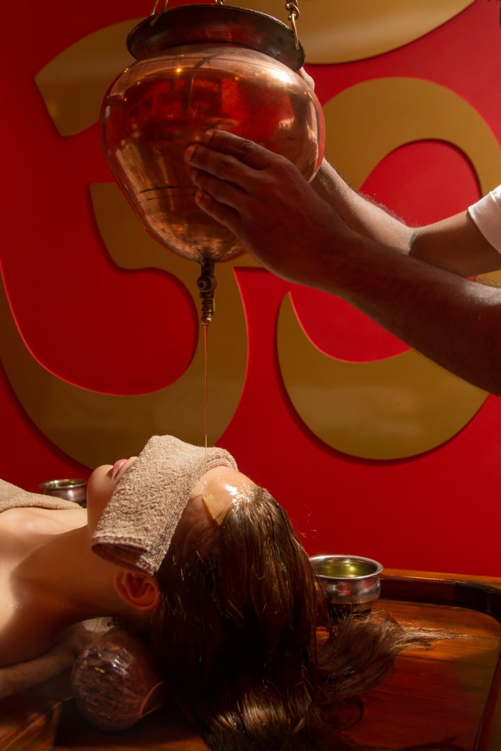 Shirodhara, an Ayurvedic healing technique. Oil dripping on the female forehead. Portrait of a young woman at an ayurvedic massage session with aromatic oil dripping on her forehead and hair.