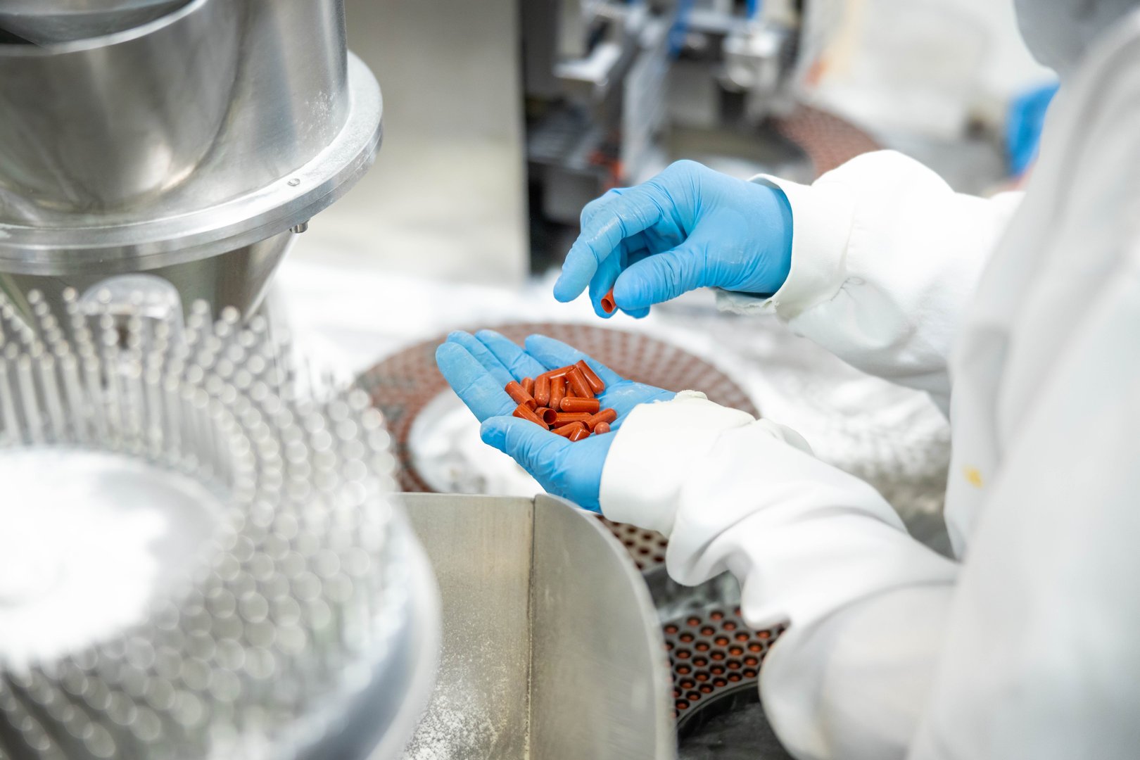 A close view of red capsules held for inspection before production, focusing on the emphasis of health safety in pharmaceuticals.