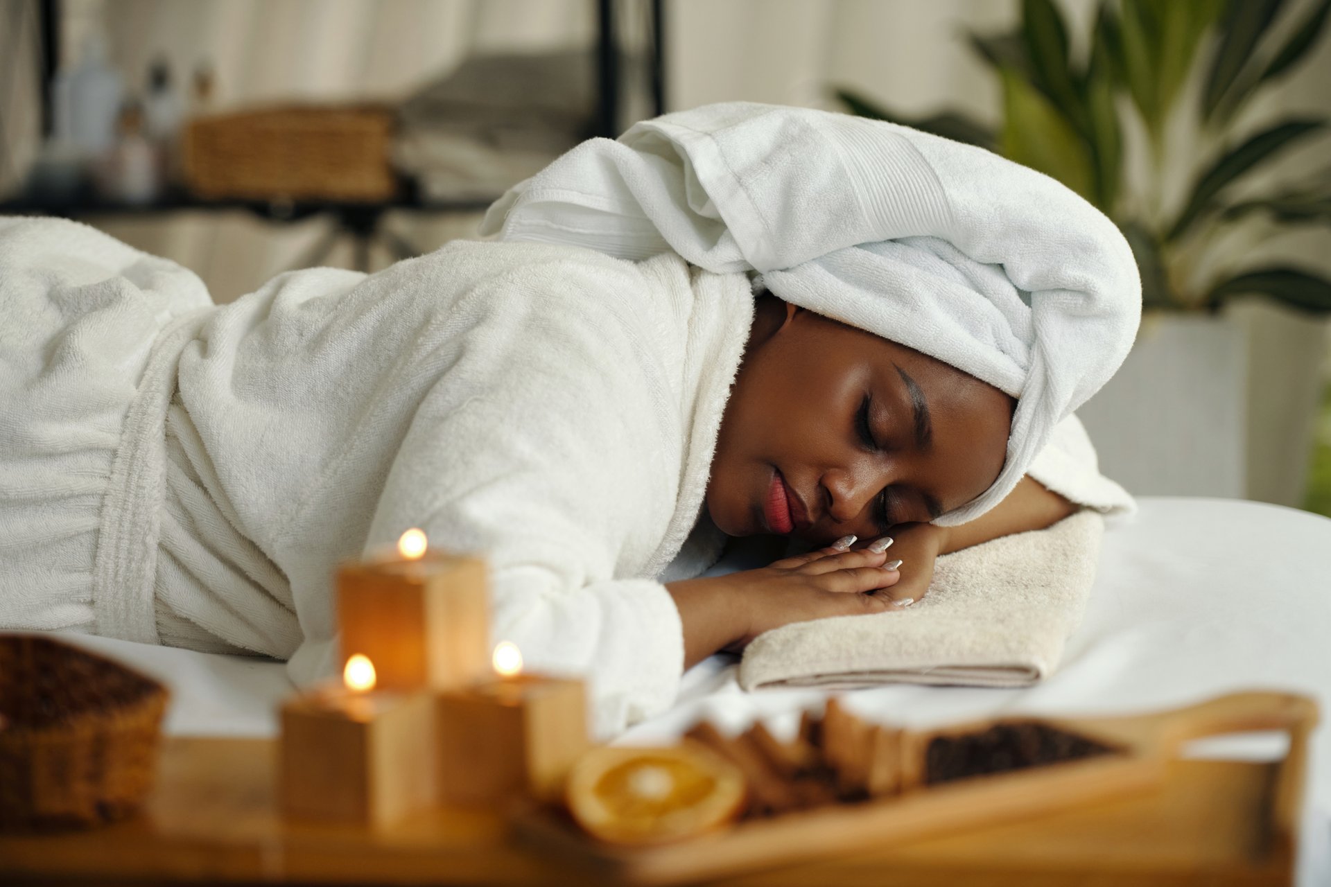 Relaxing at spa wrapped in towel with candles and massage tools in foreground creating a peaceful ambiance breathing softly in soothing environment with fragrant candles