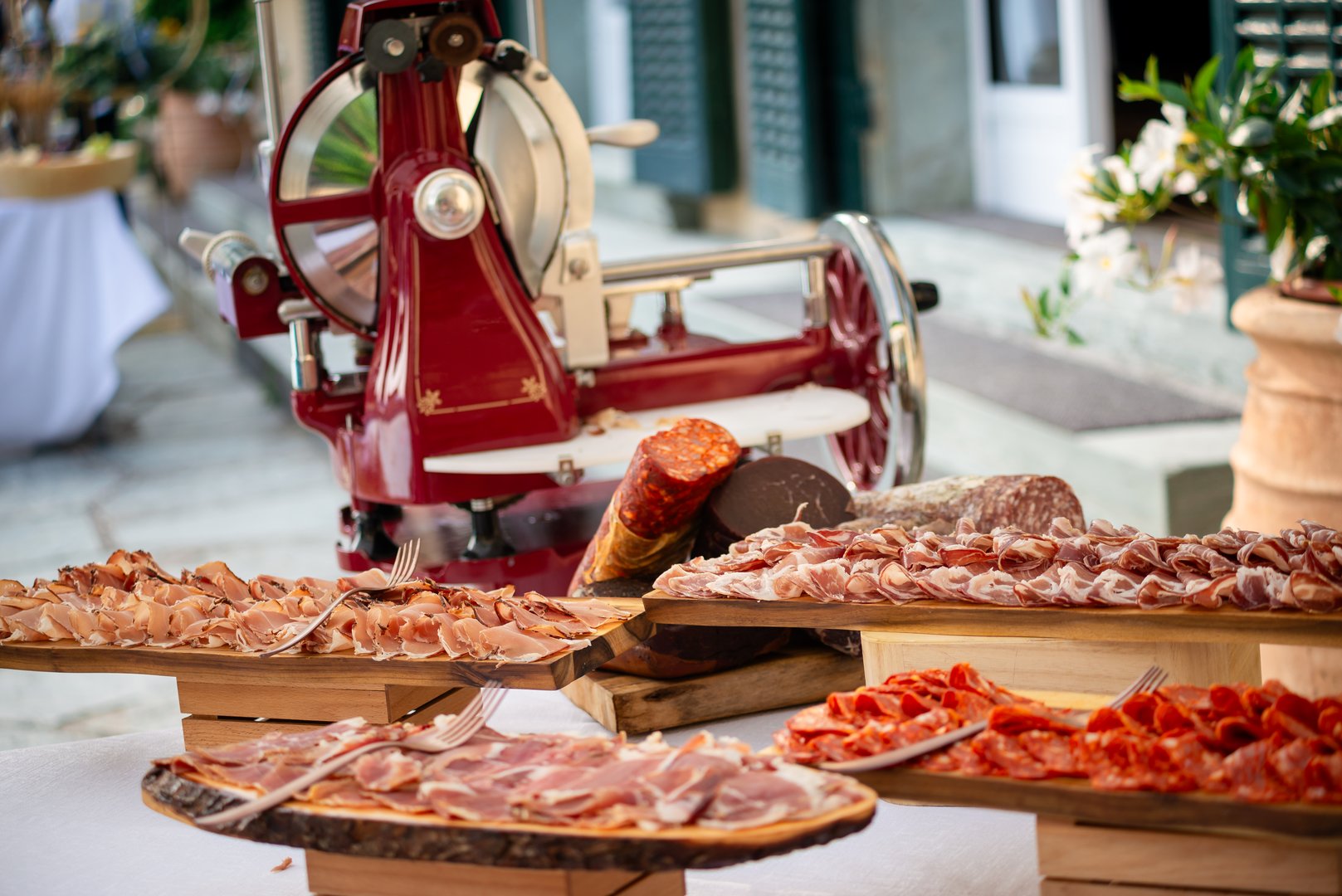 A charcuterie table showcases various cured meats at a wedding reception, with a vintage slicer adding charm to the elegant setting.
