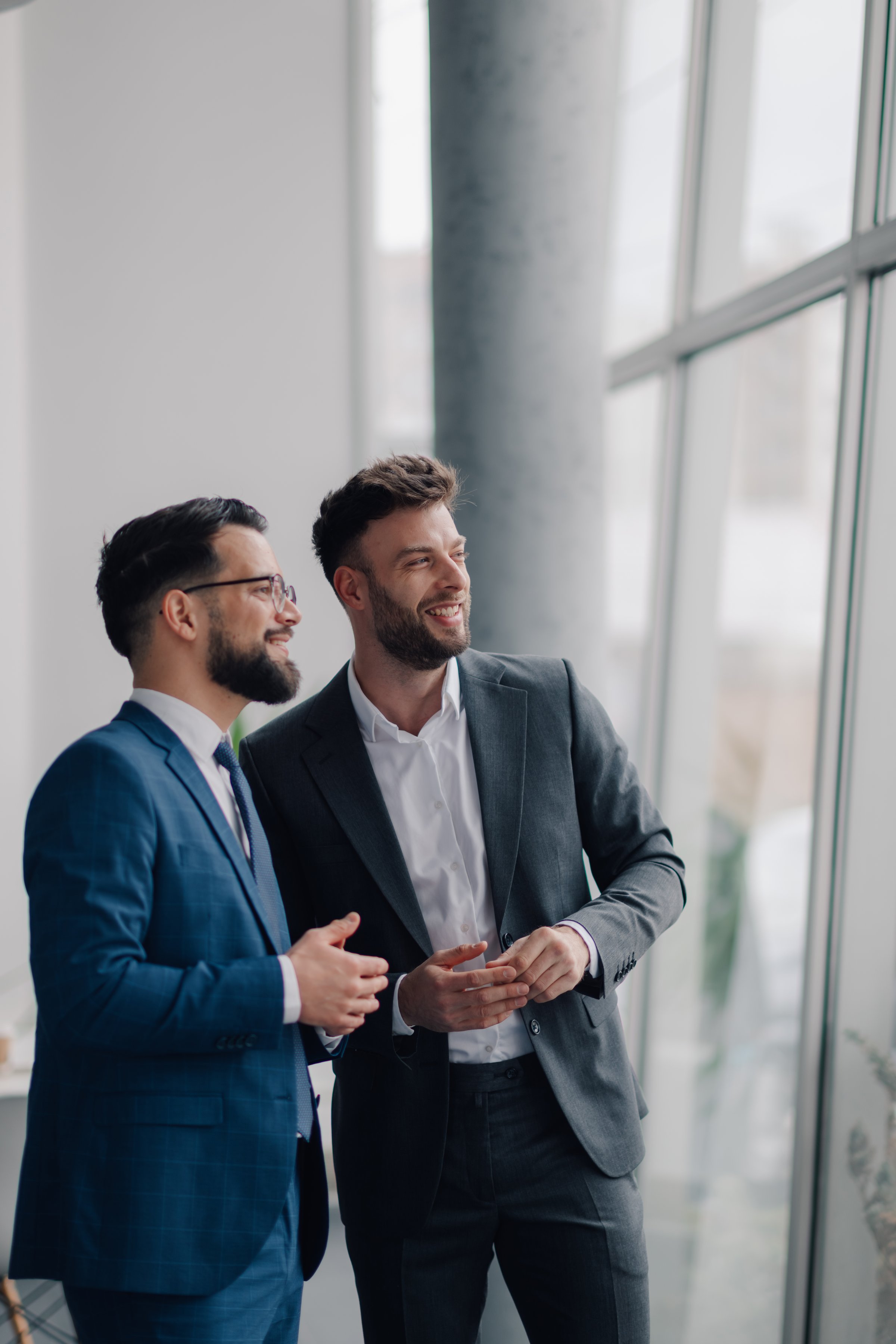 Two businessmen are discussing strategy and smiling near window in modern office