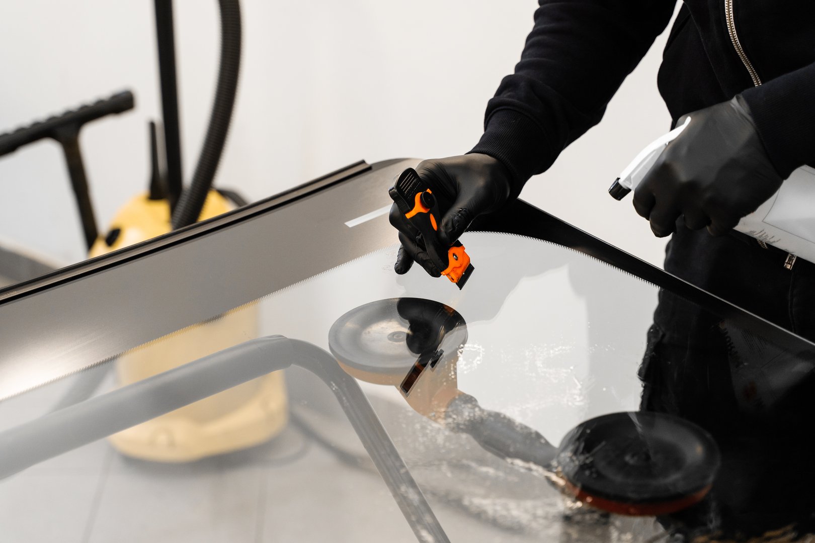 Technician uses scraper to clean the surface of a new windshield post-replacement. Technician scrapes and cleans new windshield after replacement to ensure perfect adhesion